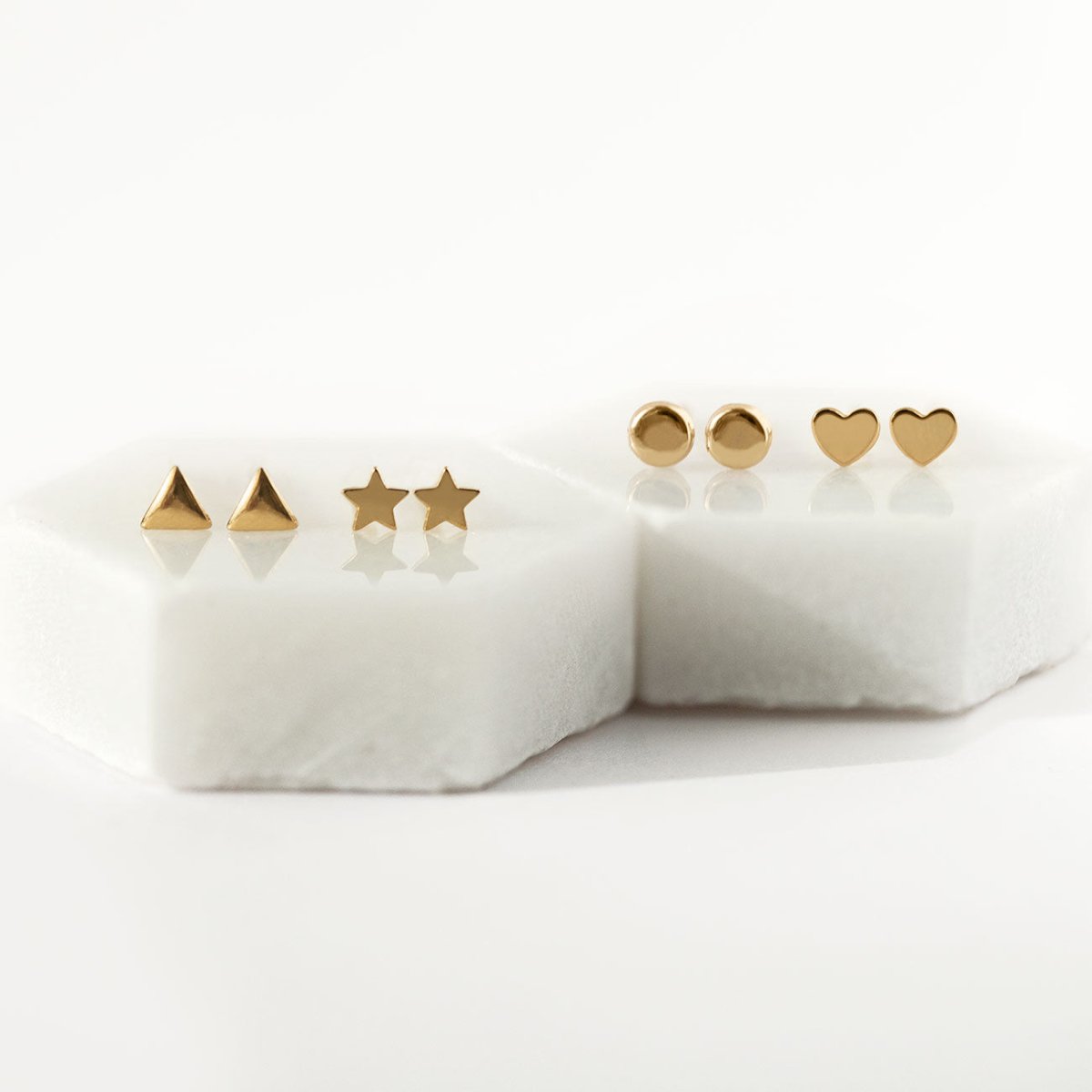 Gold triangle, star, round disc and heart stud earring pairs displayed on white marble