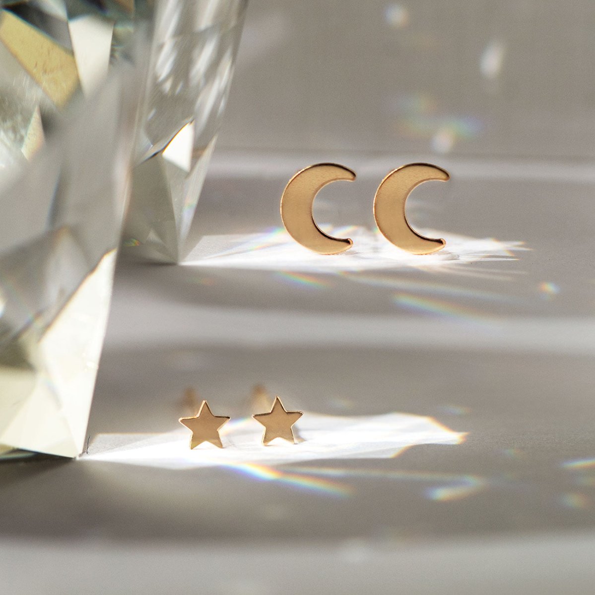 Gold-filled crescent moon studs and star studs resting near a crystal on a soft surface