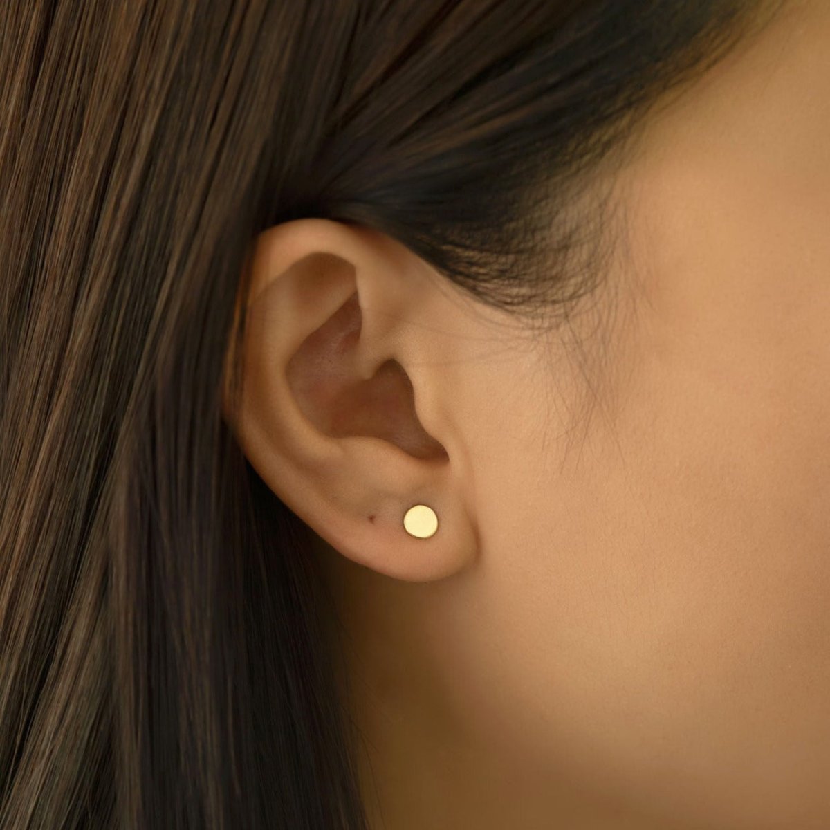 14K gold flat round disc stud earring shown on a model's lobe, close-up detail