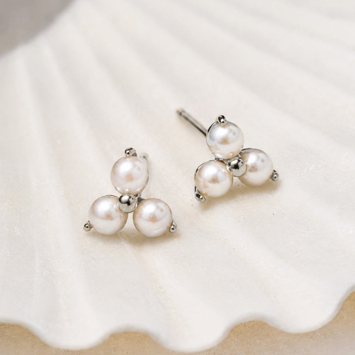 Pearl Trinity Studs 14K White Gold featuring three freshwater pearls in a triangular design displayed on a white seashell.