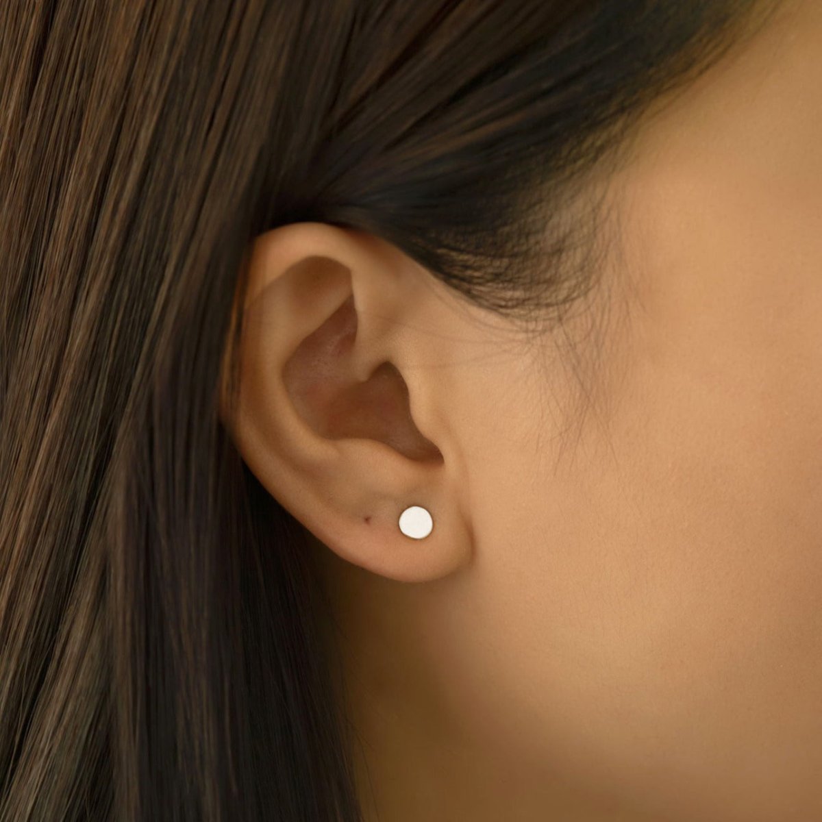 14K white gold flat round disc stud earring shown on a model's lobe, close-up detail