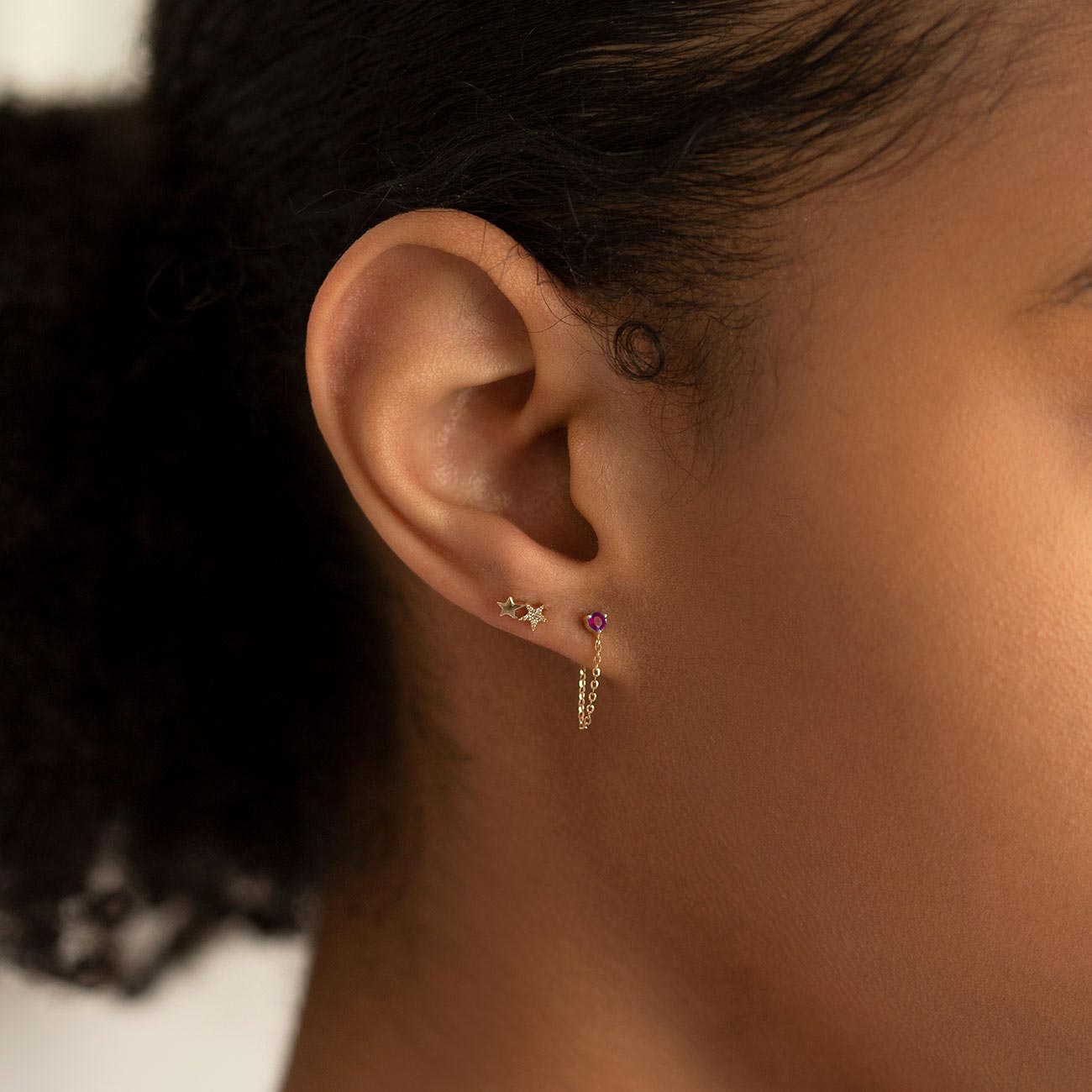 14K gold single chain stud earring with a round red ruby, shown on a model's lobe with a draped chain