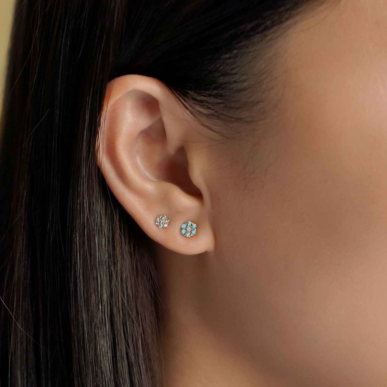 14K gold blue zircon flower cluster stud shown on a model's lobe beside a clear flower stud