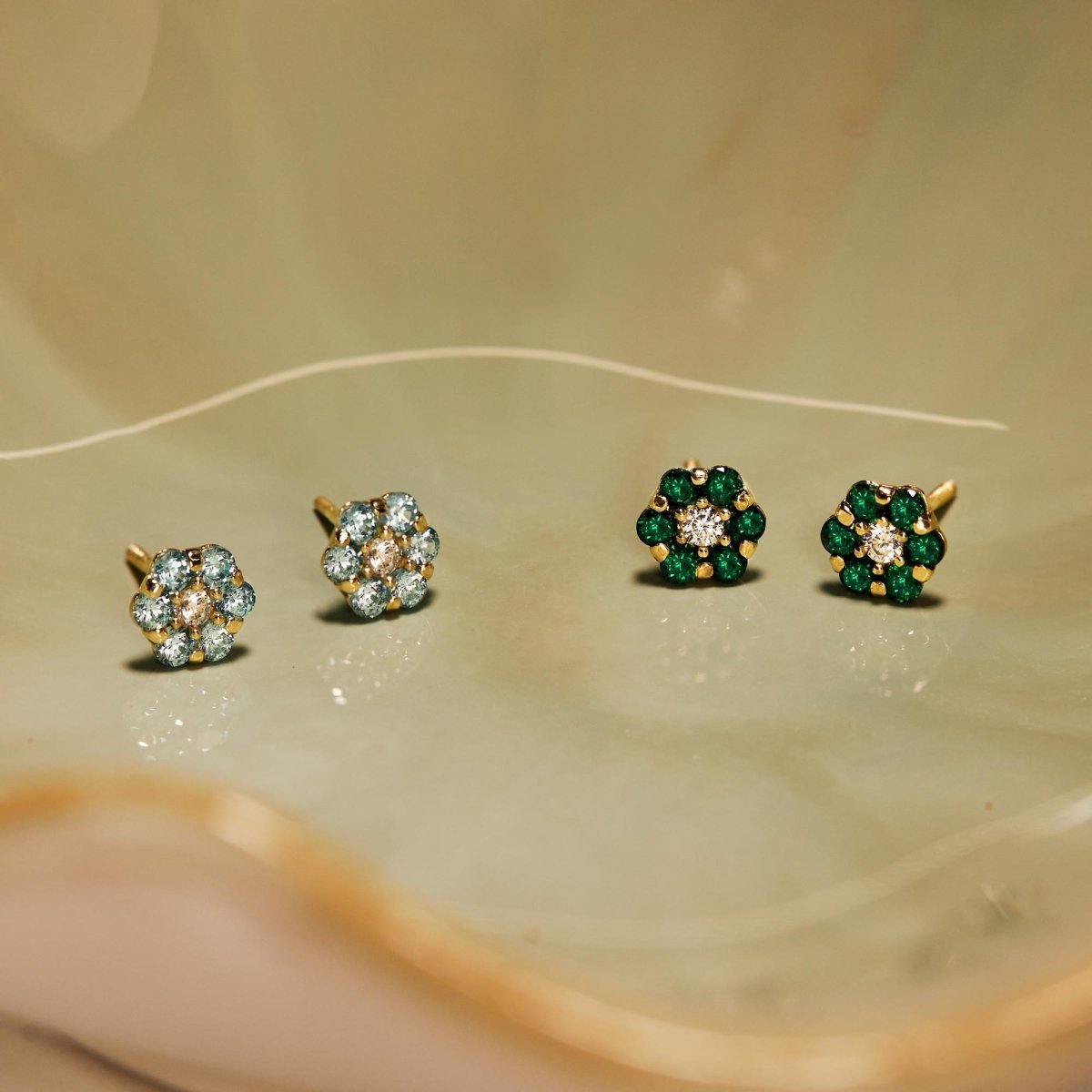 14K gold flower cluster studs with green stones arranged with other cluster pairs on a cream background