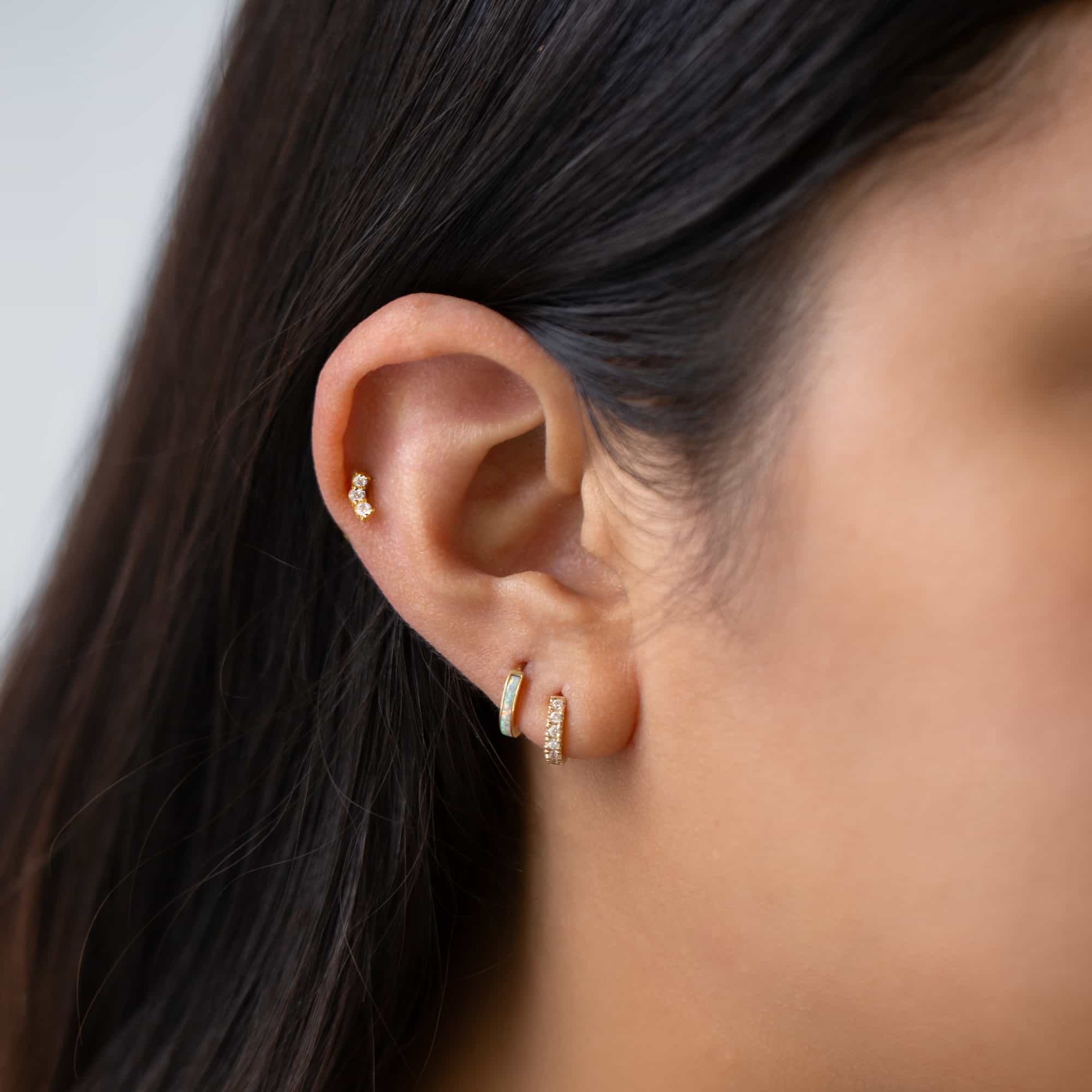 Gold vermeil flat back stud with three curved white zirconia stones, shown on a model's ear stack