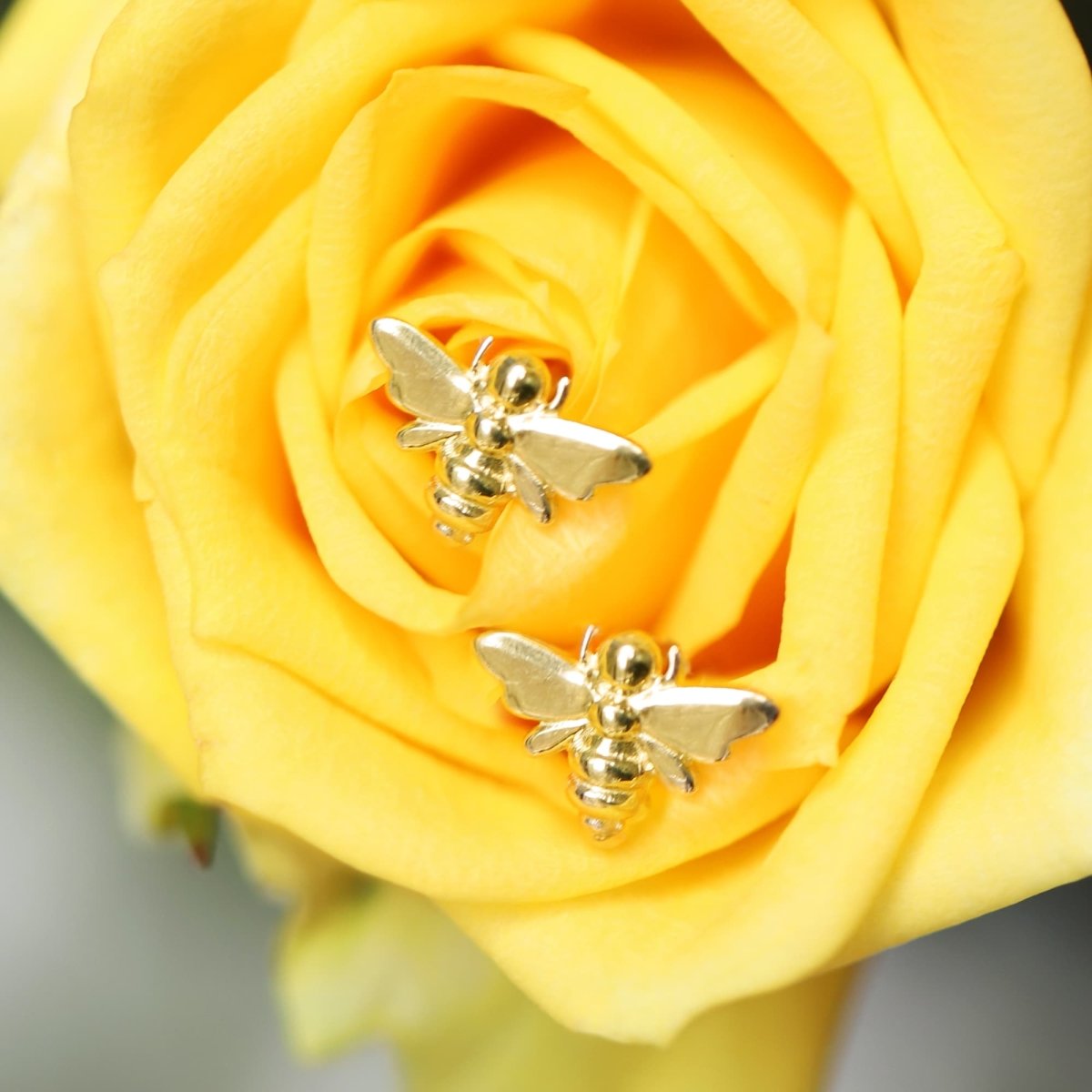 Pair of 14K gold mini bee studs nestled in a yellow rose, close-up detail