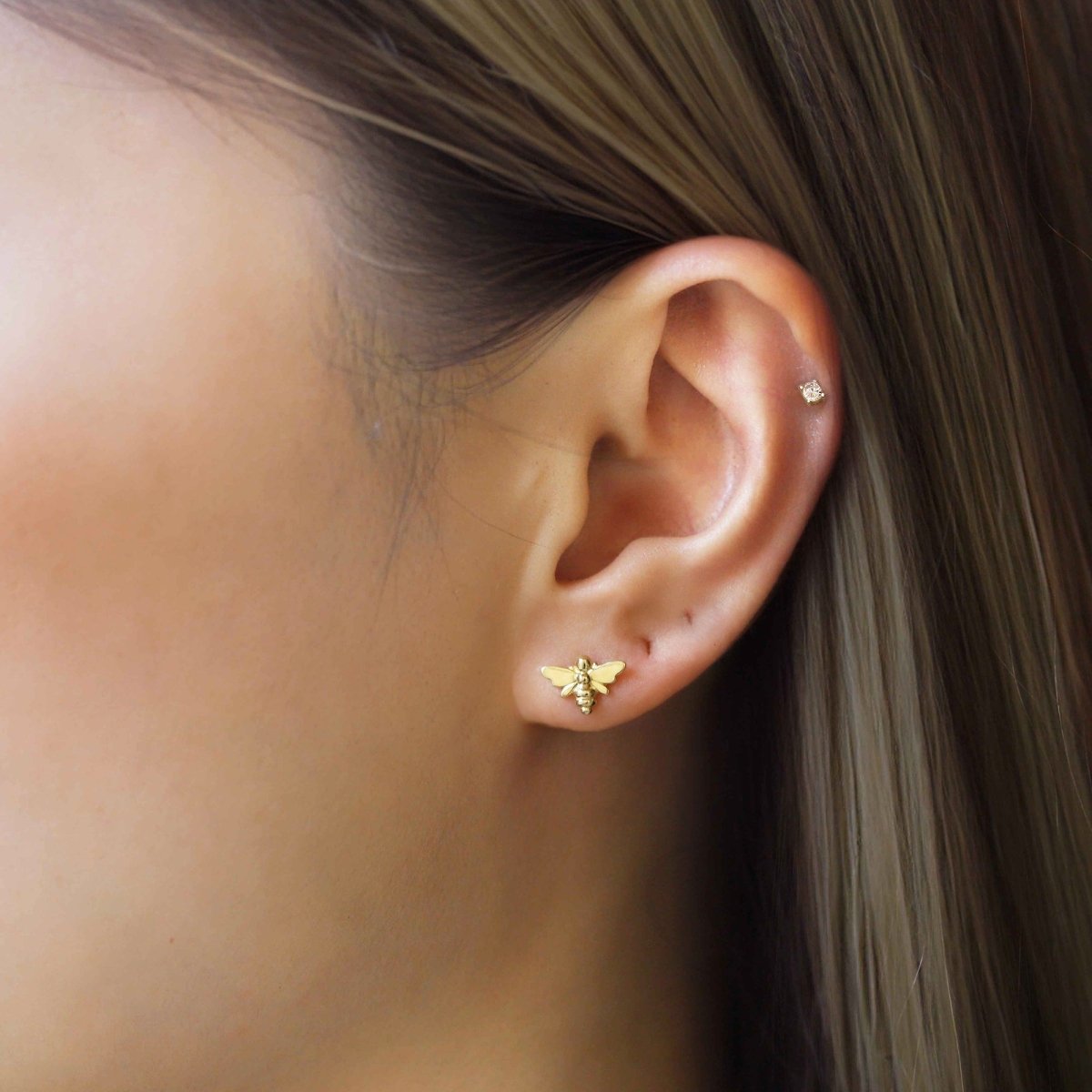 14K gold mini bee stud shown on a model's lobe with a tiny stud in the helix