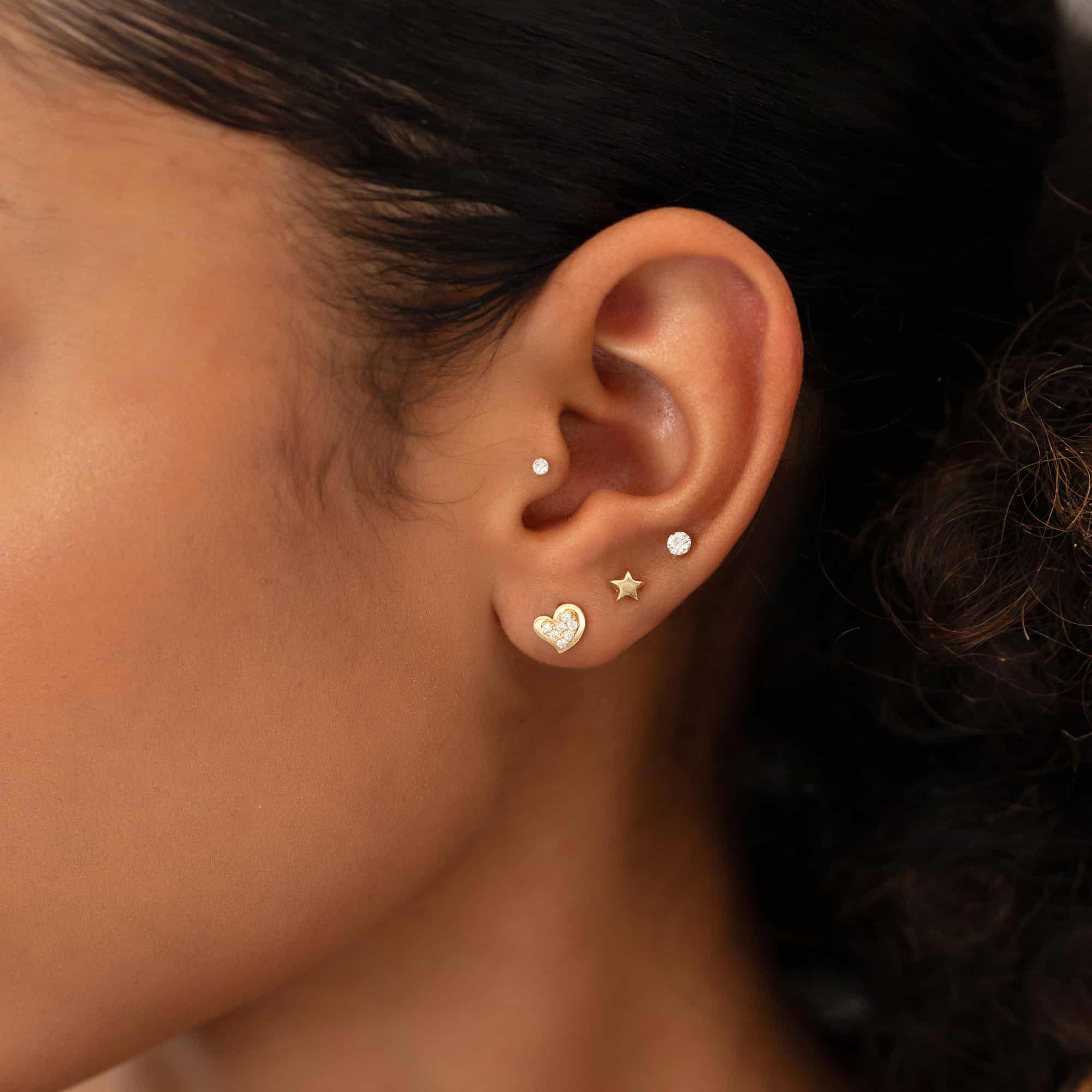 14K gold pavé heart stud with white zirconia shown on a model's lobe in an ear stack
