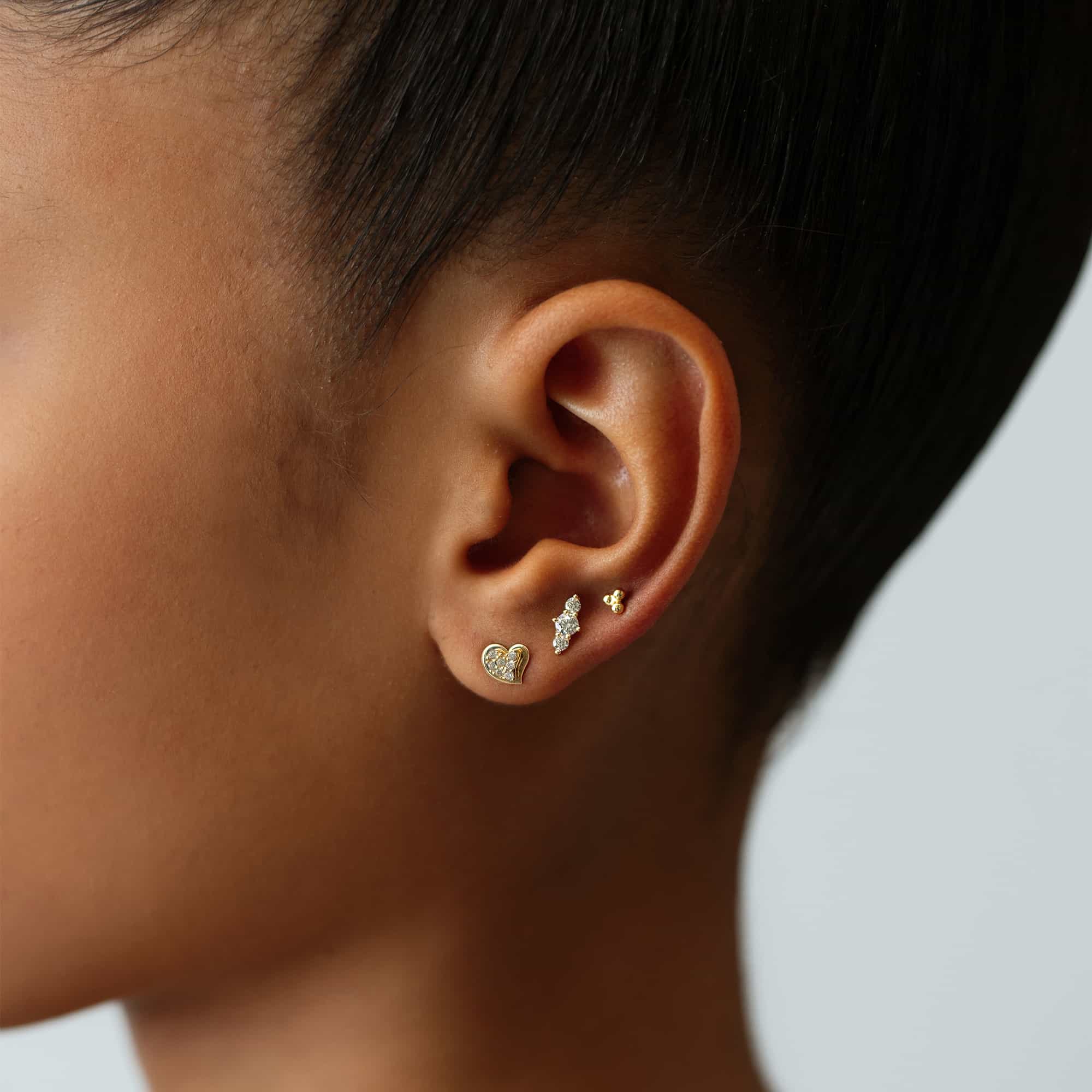 14K gold pavé heart stud with white zirconia shown on a model's lobe beside a cluster stud