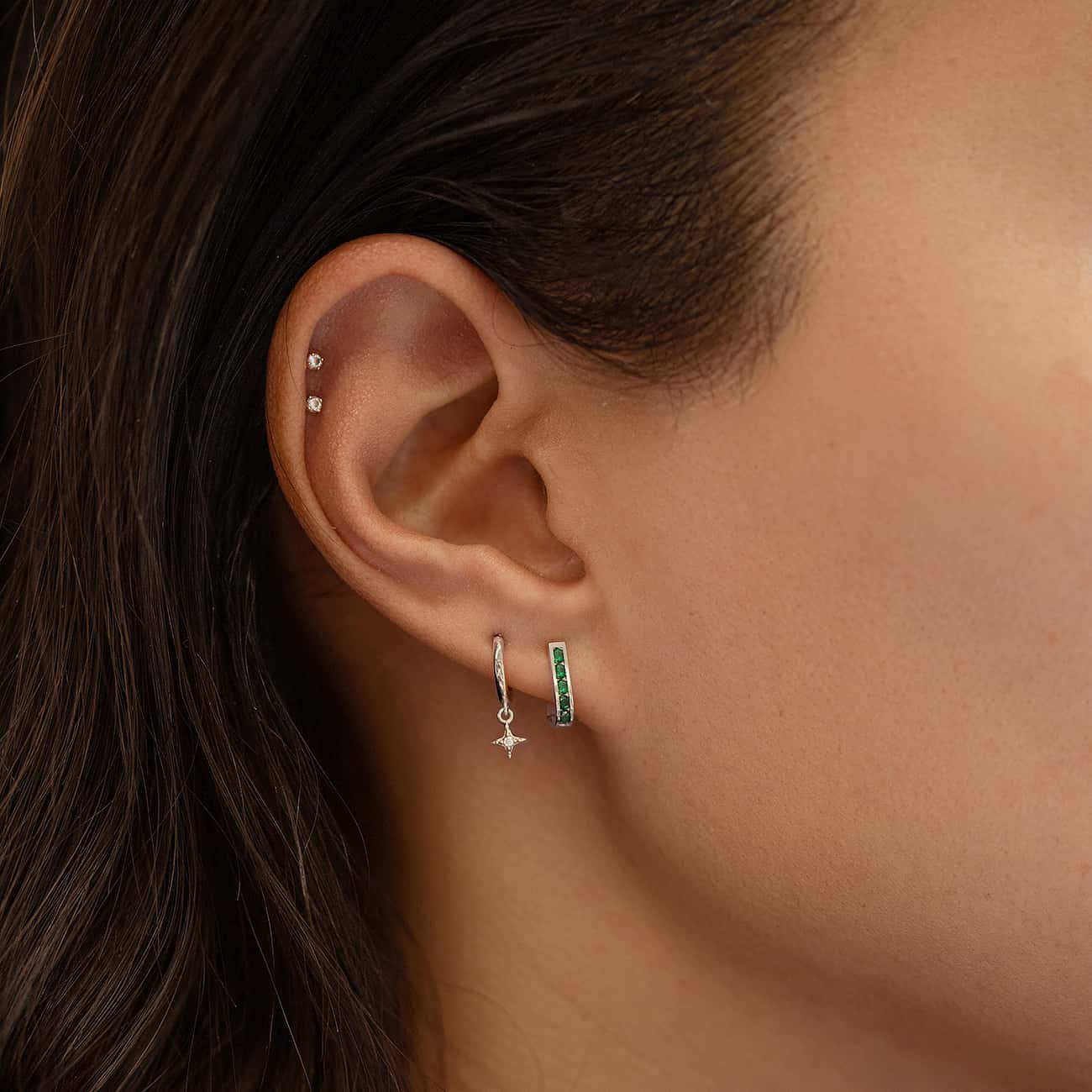 14K white gold emerald huggie hoop with green stones, shown on a model's lobe in an ear stack