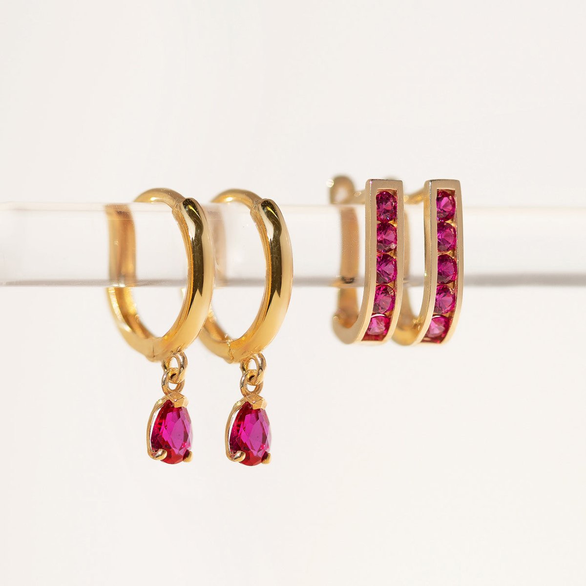 14K gold ruby huggie hoops shown beside dangling pink teardrop-stone hoops, close-up detail