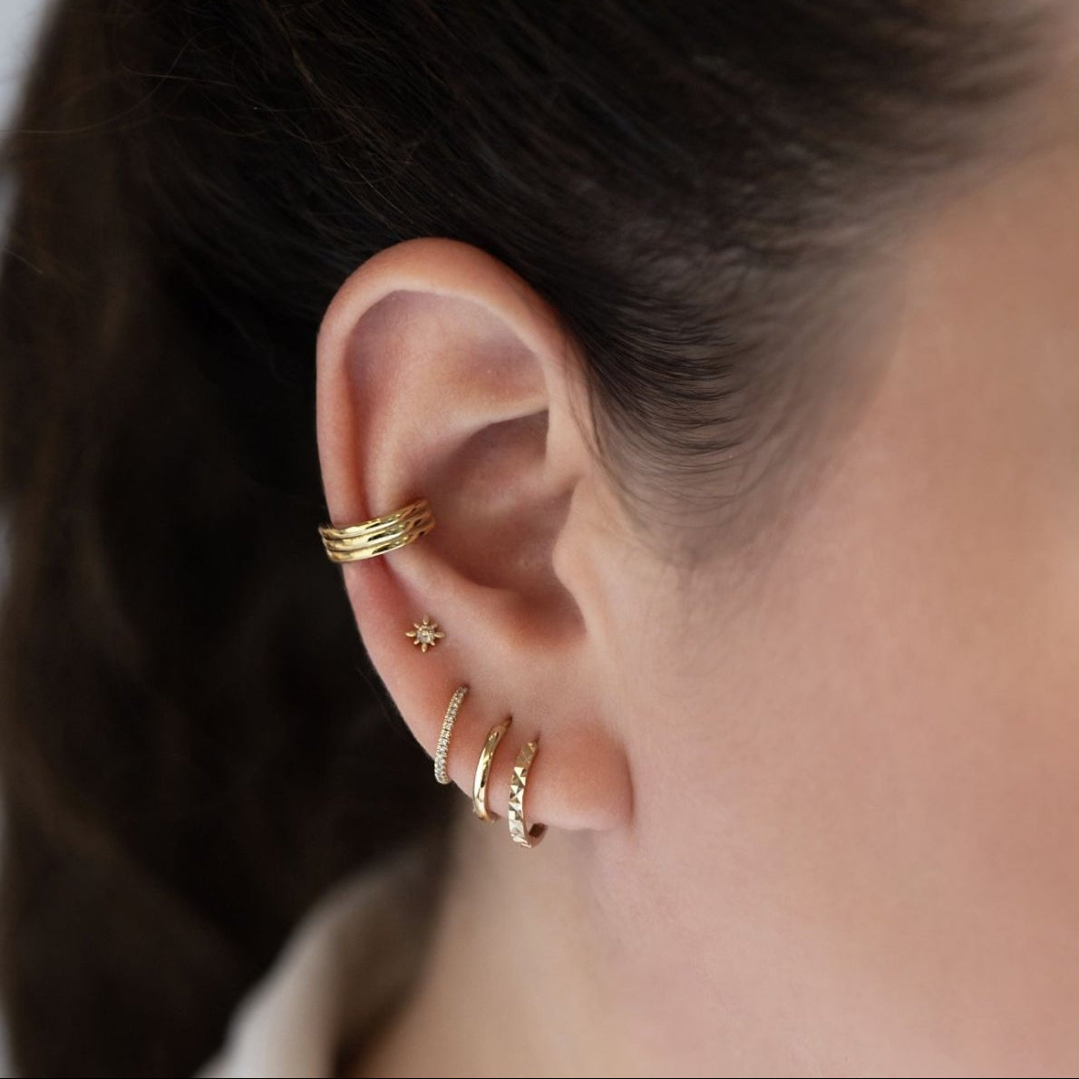 Gold star stud, hoops, and a beaded ear cuff styled on a model's ear