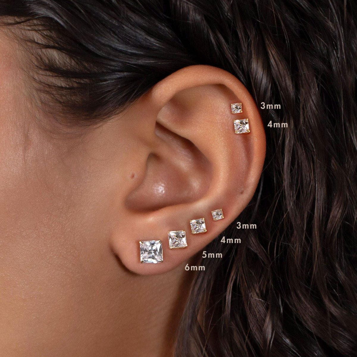 14K white gold princess-cut clear stone studs, size comparison 3mm, 4mm, 5mm and 6mm on a model's ear