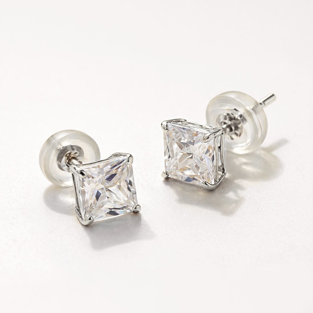 14K white gold princess-cut studs with square clear stones and clear backs, close-up detail on a cream background