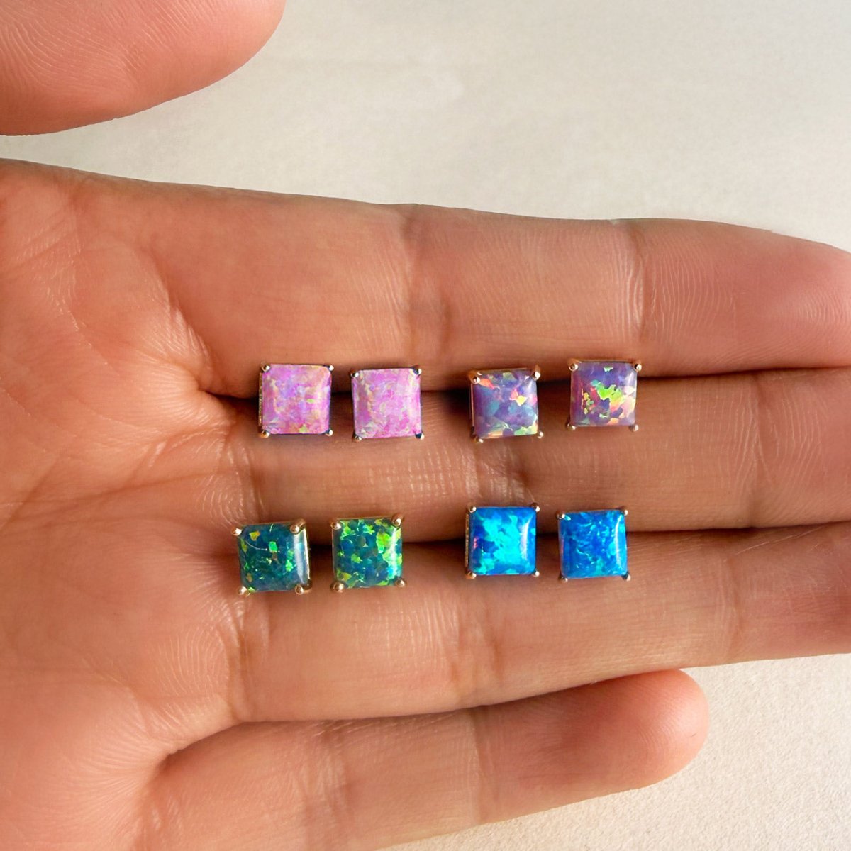 14K gold square opal-look studs in pink, green and blue held on a hand for size