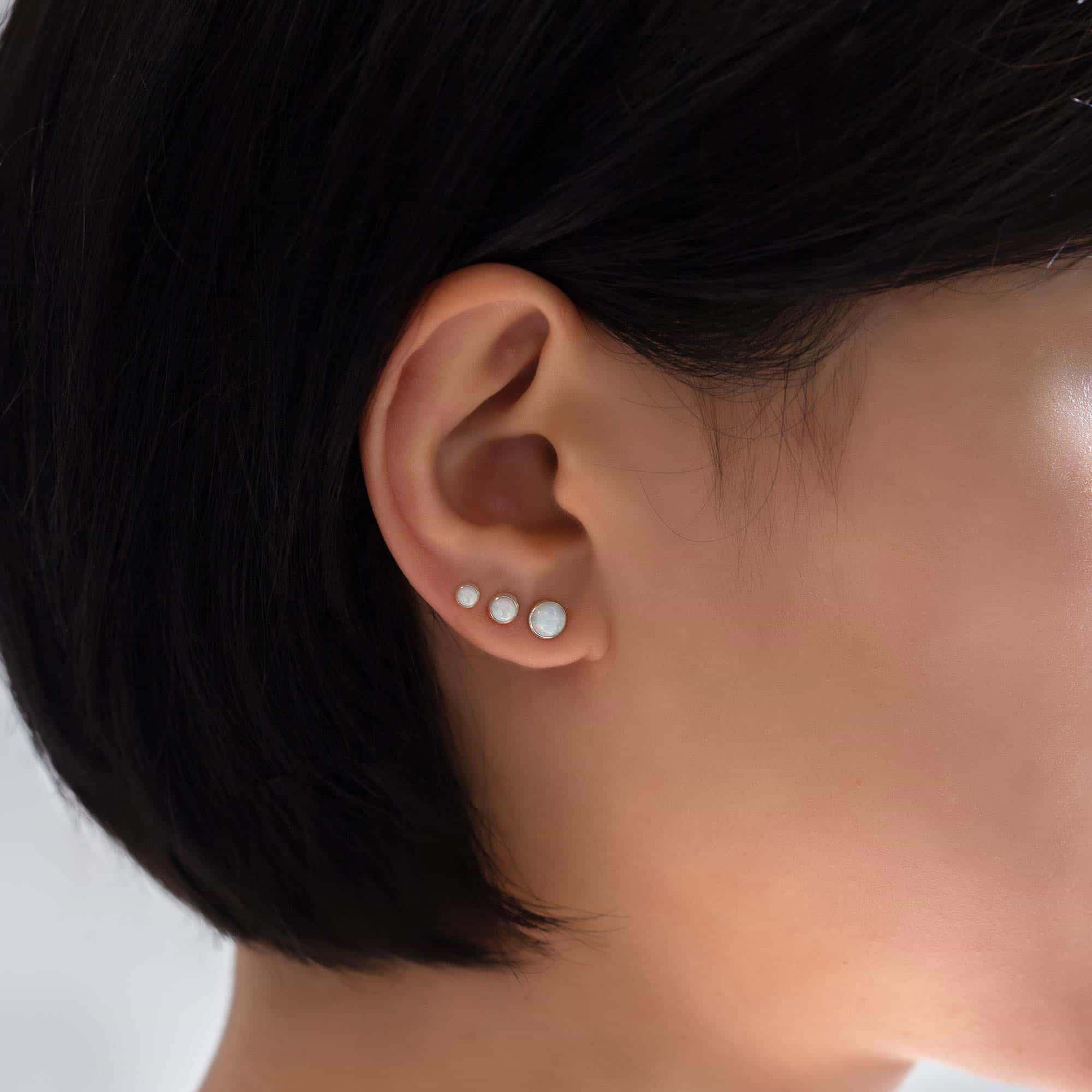 14K white gold tiny white opal cabochon studs shown in a three-stud row on a model's lobe