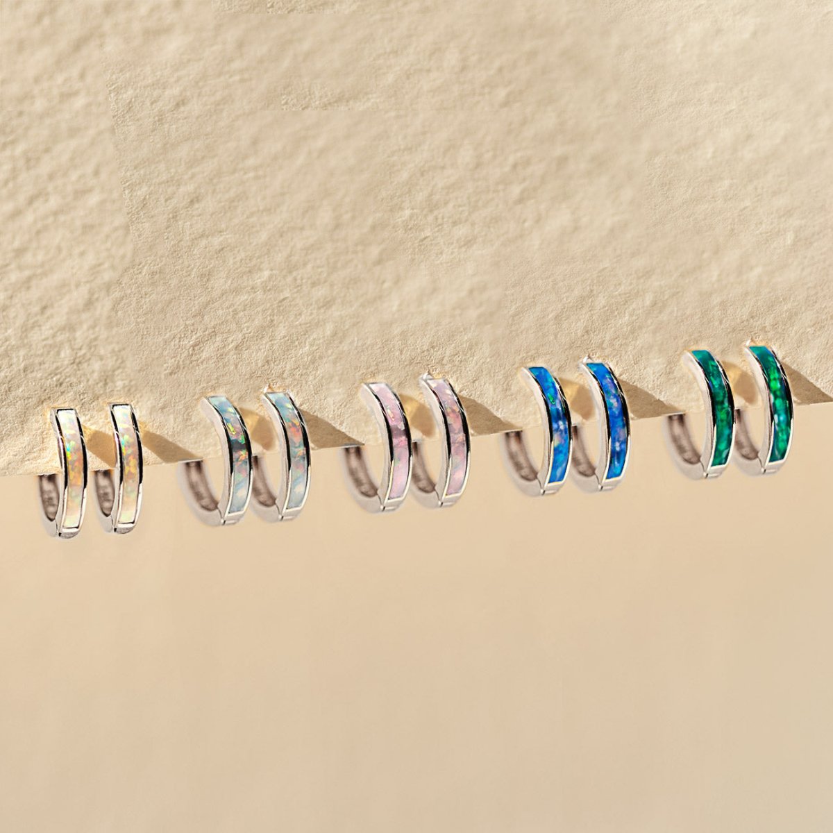 14K white gold inlay huggie hoops in white, pink, blue and green, lined up on a cream background