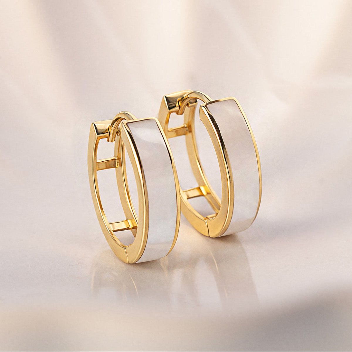 14K gold mother of pearl huggie hoops with a white inlay, close-up detail on a cream background