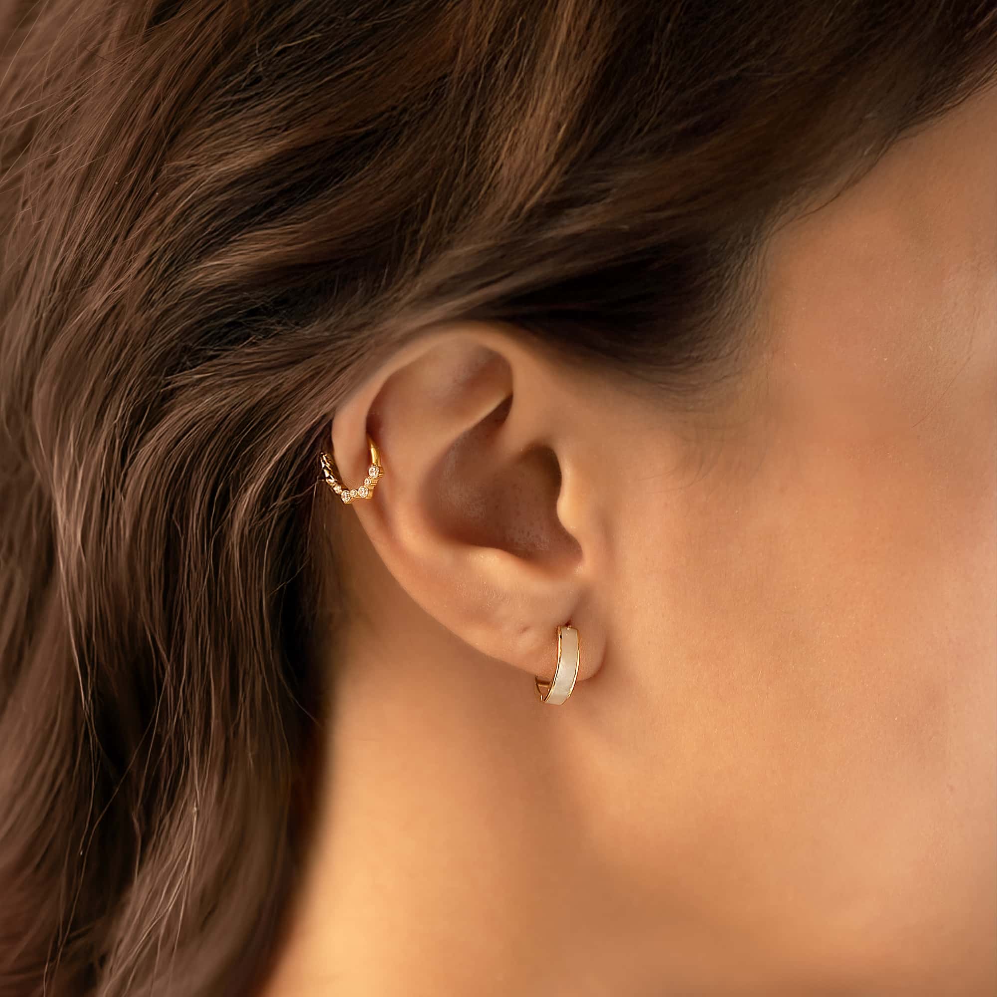 14K gold mother of pearl huggie hoop with a white inlay, shown on a model's lobe with an ear cuff above