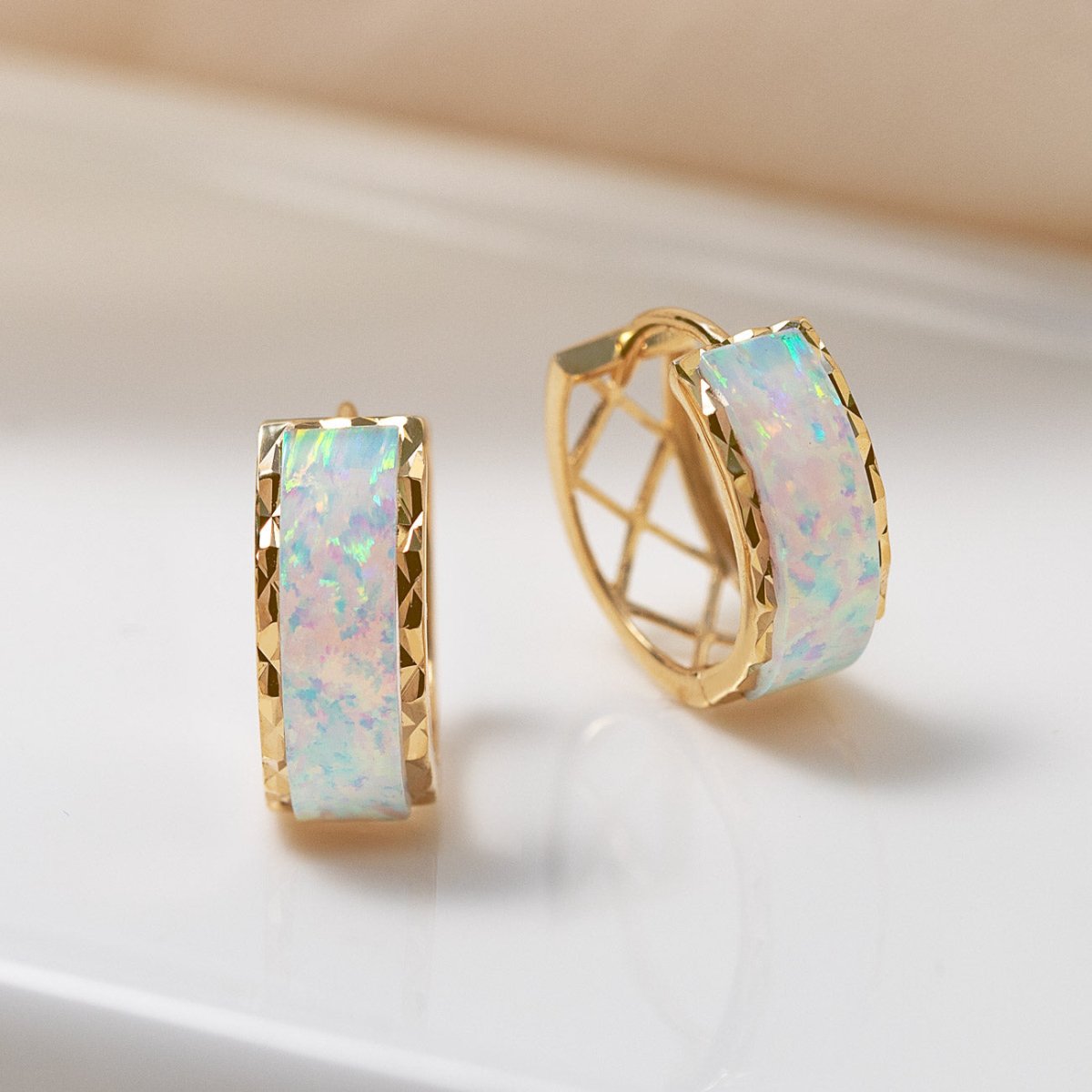 14K gold chunky huggie hoops with iridescent white opal inlay, close-up detail on a cream background