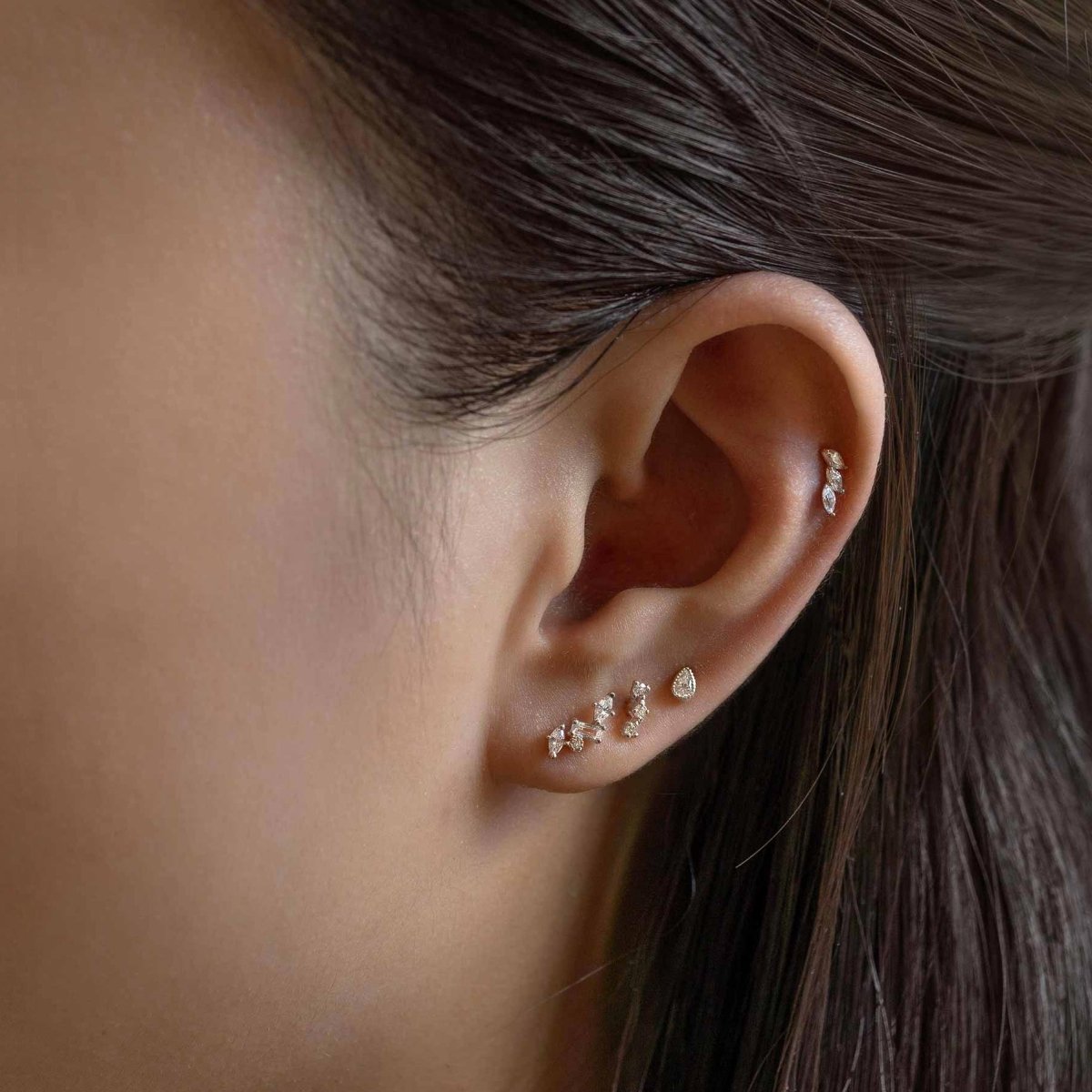Sterling silver tiny marquise curve studs with clear stones, shown along a model's lobe and helix