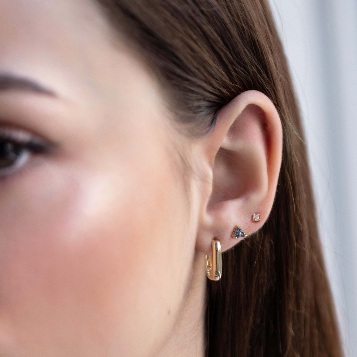Close up of woman's ear featuring Gold Vermeil Birthstone Studs Set Blue Sapphire and chunky rectangular earring 