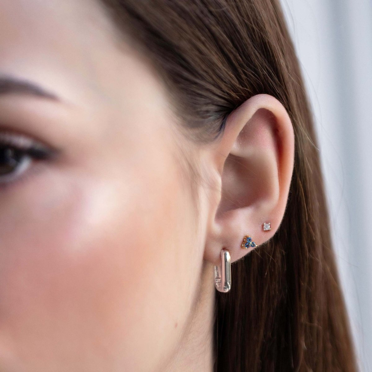 Close up of woman's ear featuring Sterling Silver Birthstone Studs Set Blue Sapphire and chunky rectangular earring 