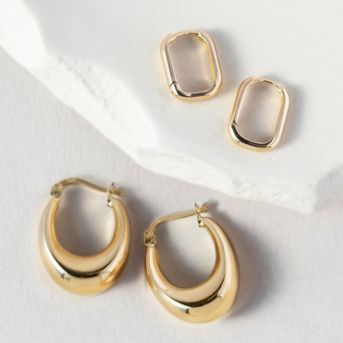 14K gold U-shaped huggie hoops shown above rounded domed hoops on white marble
