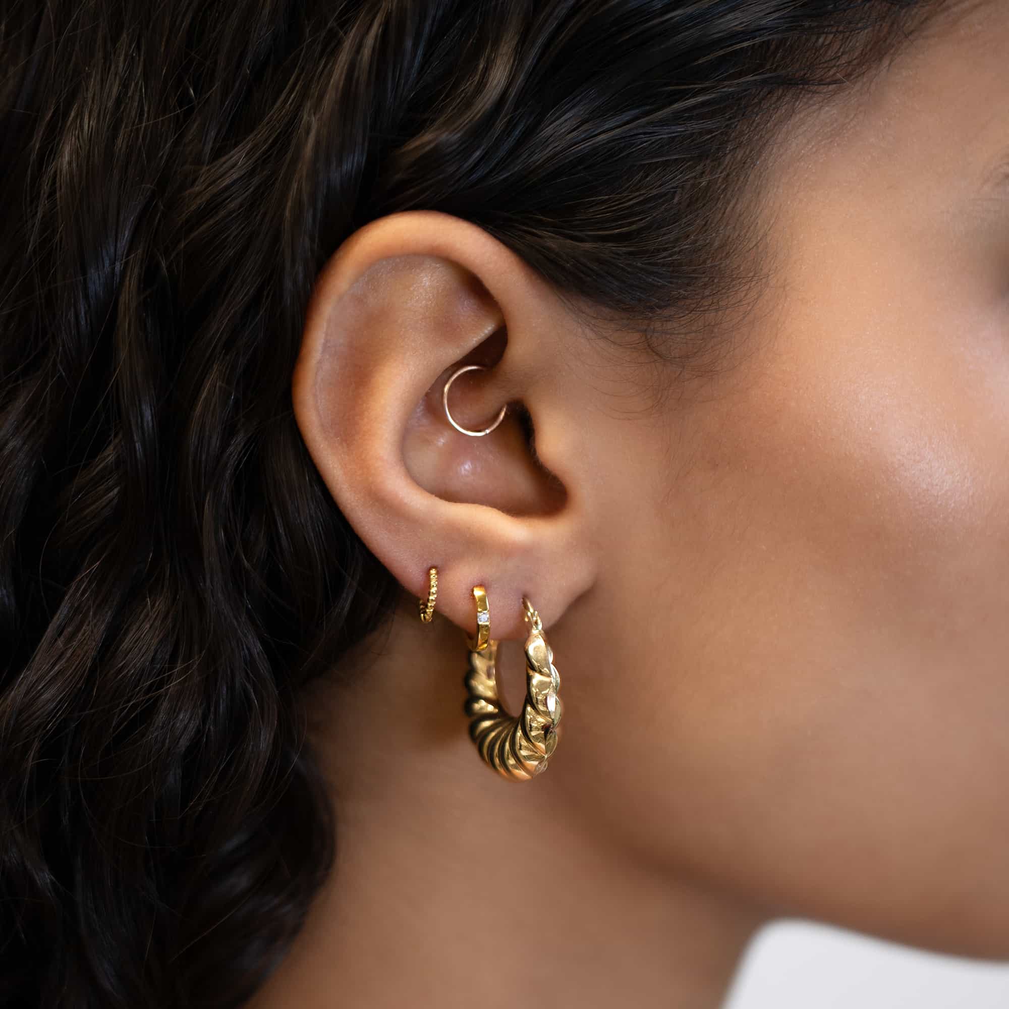 14K gold croissant bubble hoop shown on a model's lobe with stacked hoop earrings
