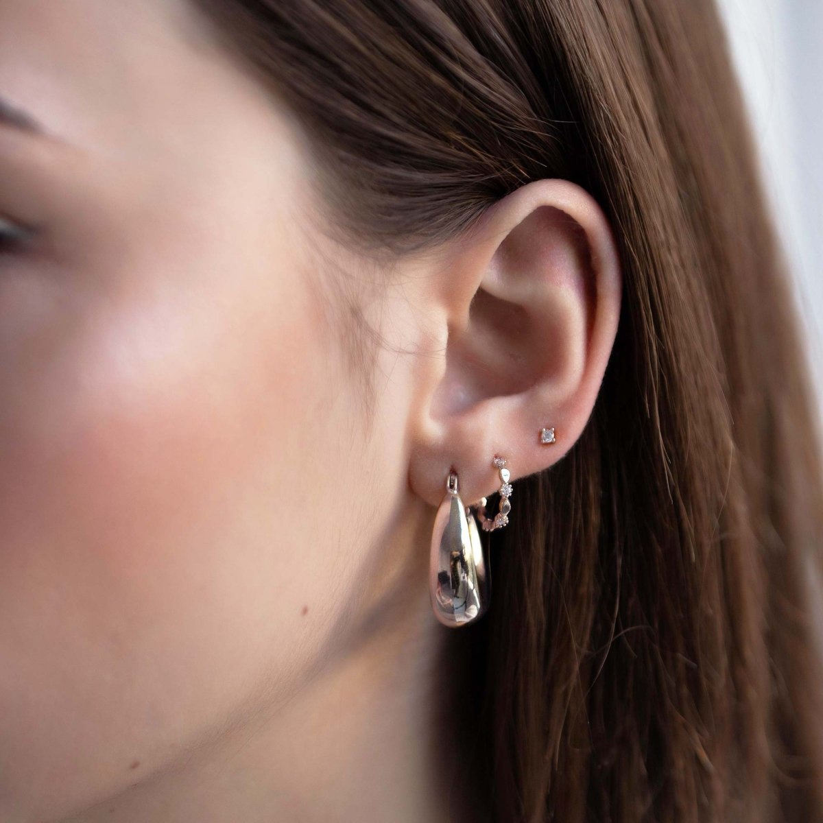Sterling silver ornate C hoop with white zirconia stones, shown on a model's lobe in an ear stack