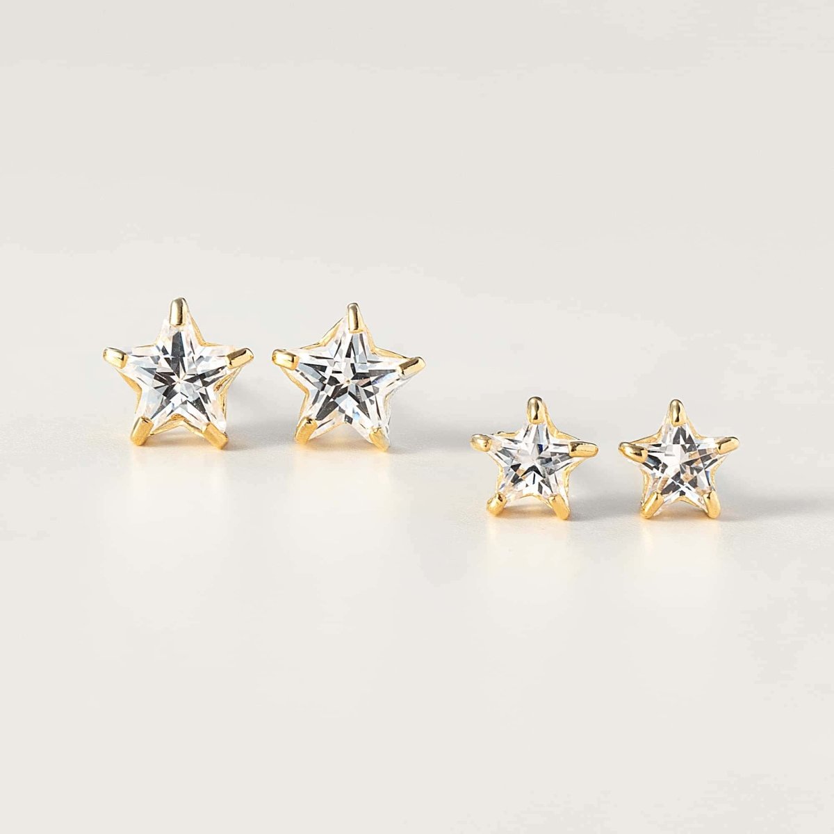 Two sizes of 14K gold star studs with faceted clear zirconia stones, on a cream background