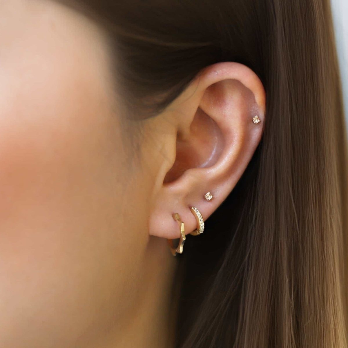 14K gold sunray ridge huggie hoop shown on a model's lobe in a stacked ear