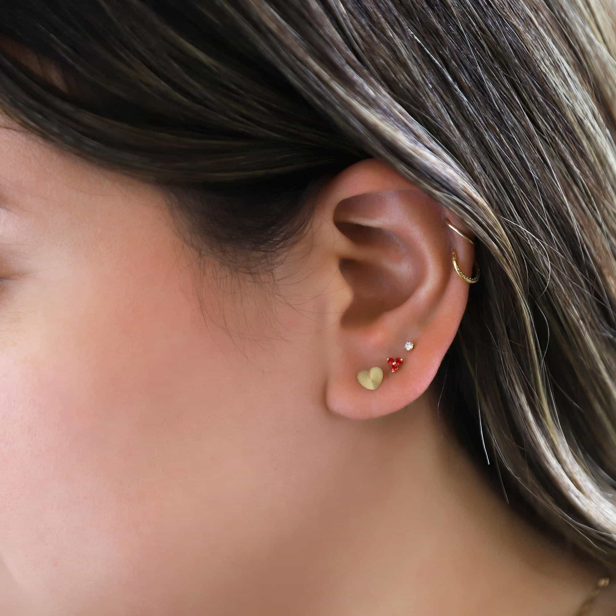 Gold heart stud with clear and red stone studs in an ear stack on a model's lobe