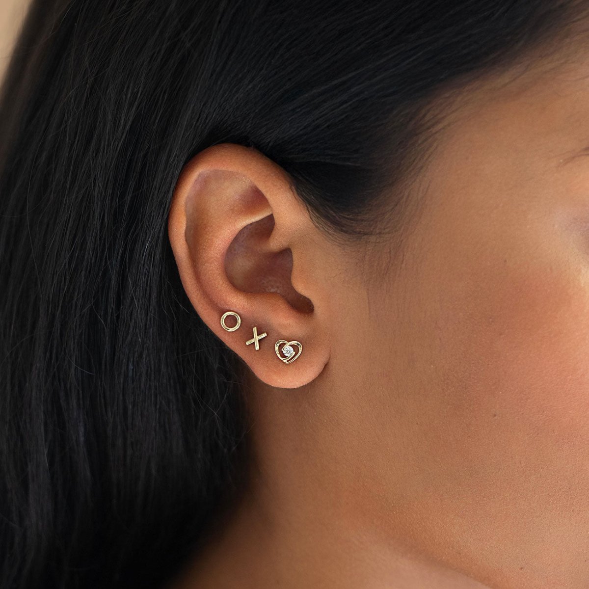 Gold X, O, and clear-stone heart studs shown on a model's lobe