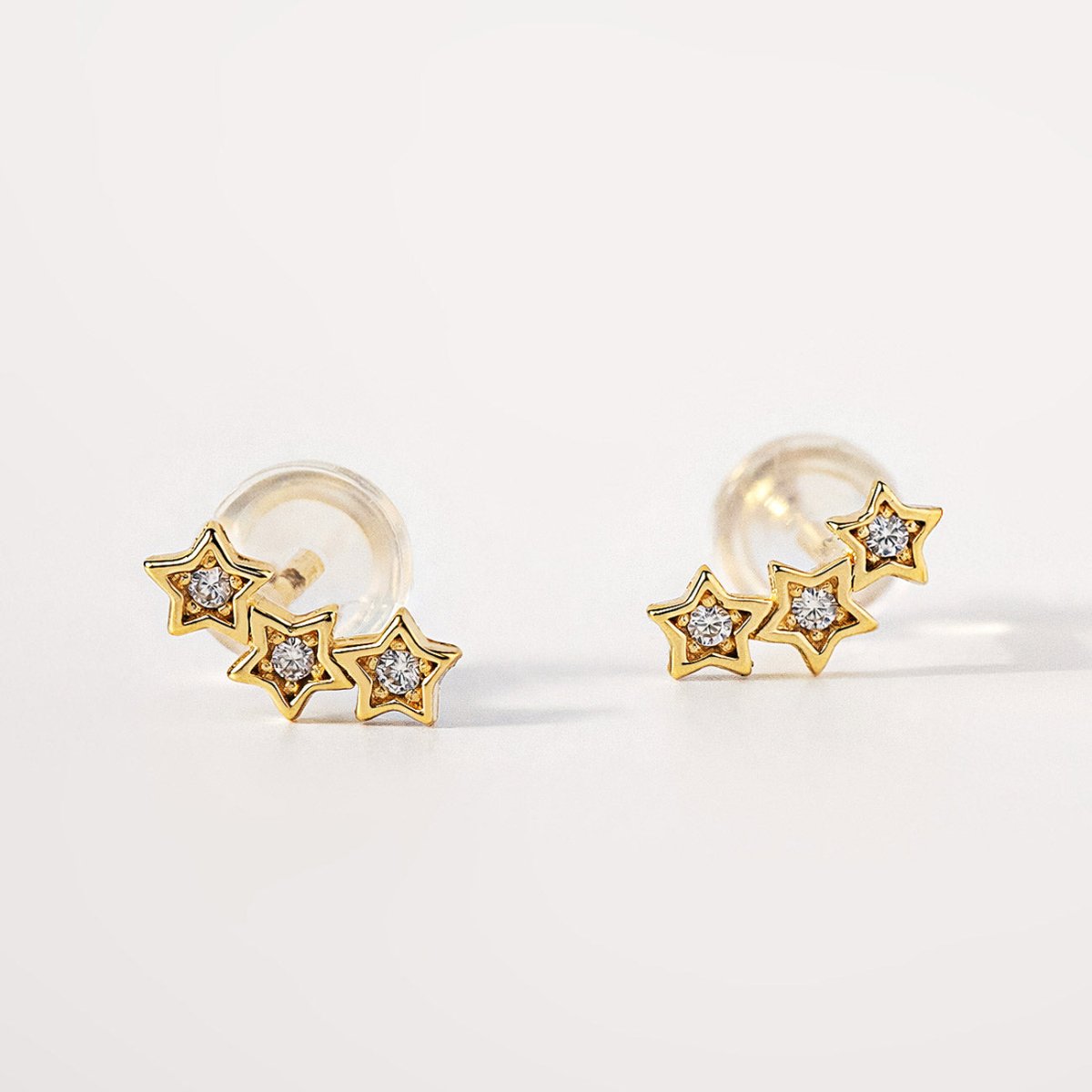 Pair of 14K gold three-star climber studs set with tiny clear stones, on a white background