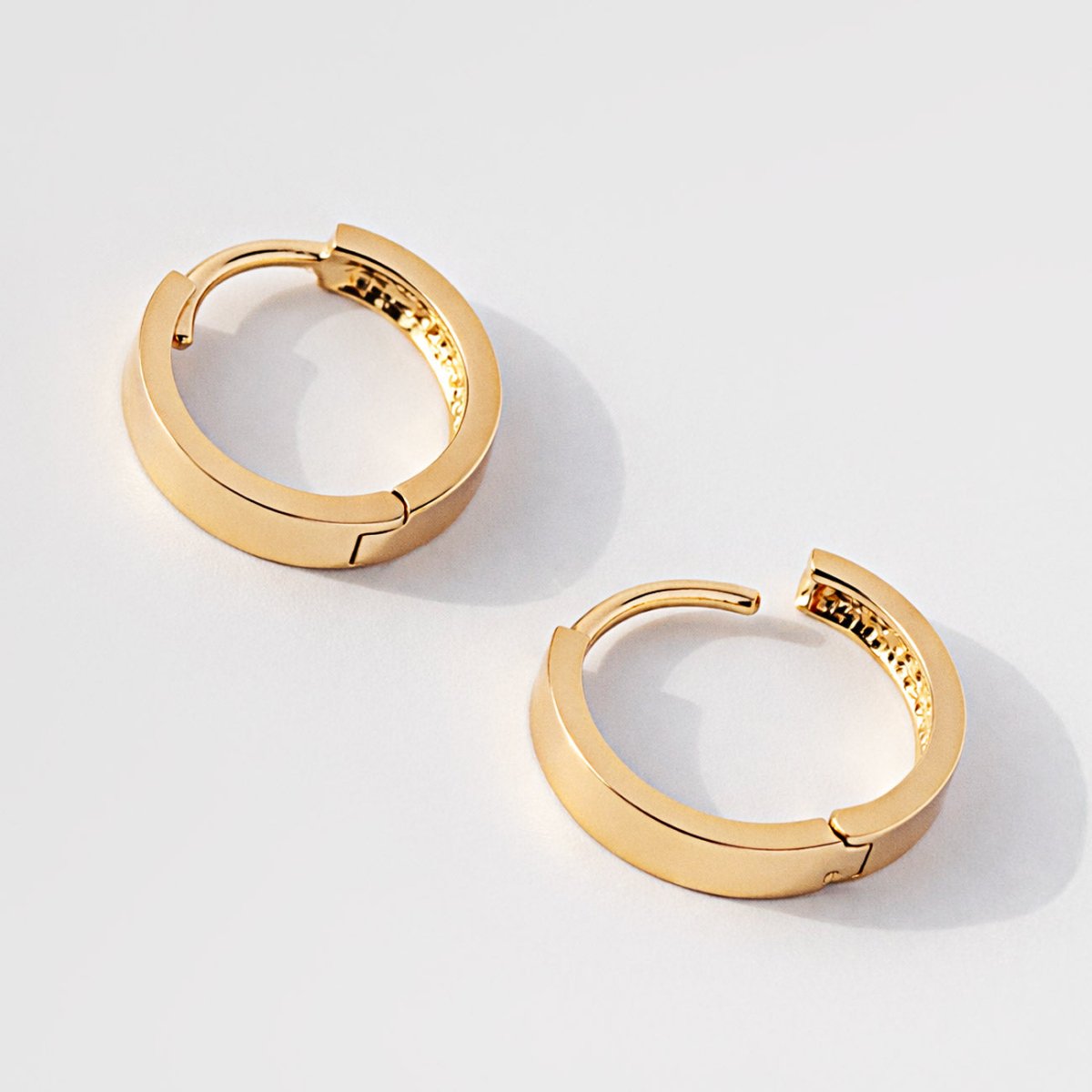 14K gold flat boyfriend huggie hoops, one open showing the hinge, on a white background