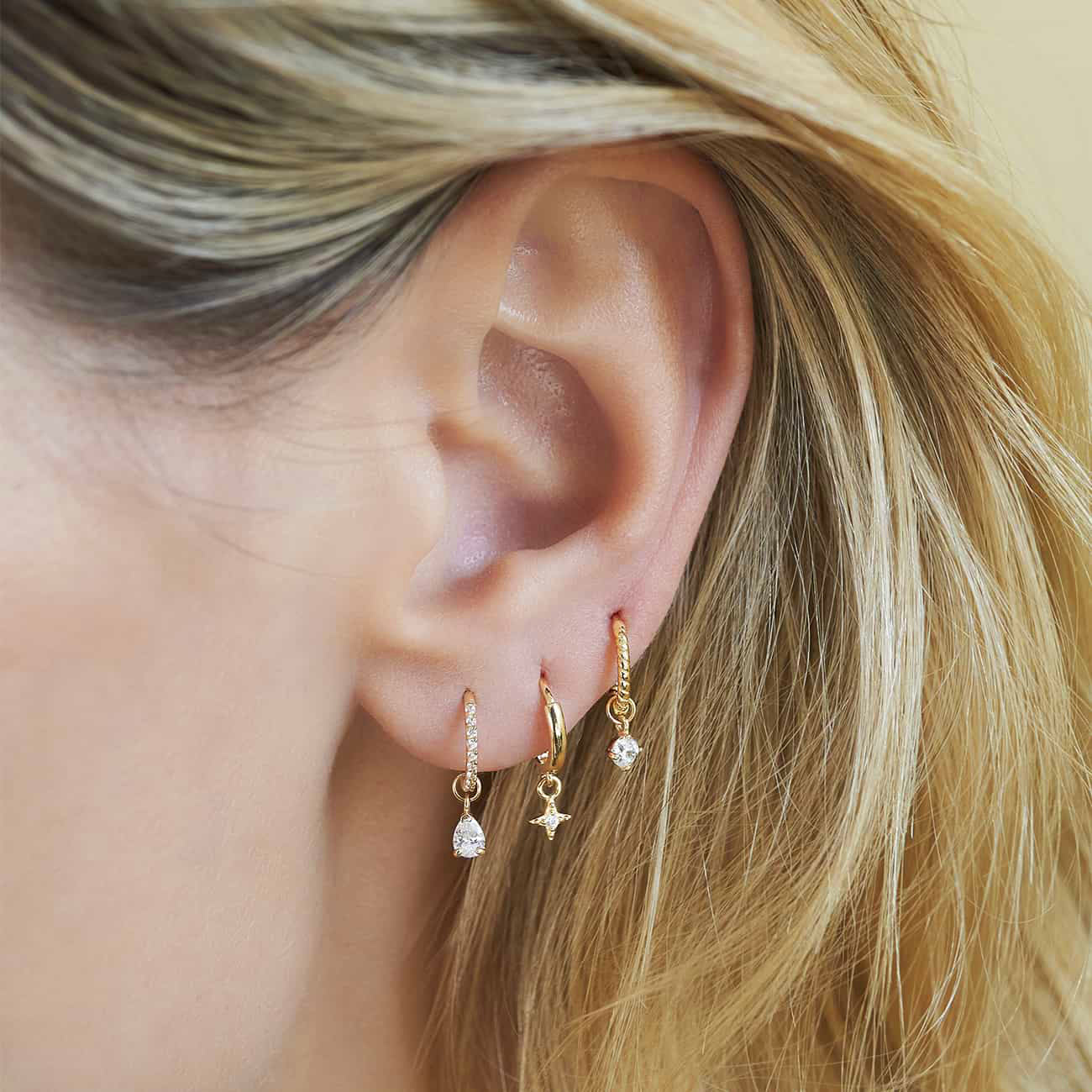 14K gold pear moissanite charm on a pavé huggie, styled in an ear stack on a model's lobe