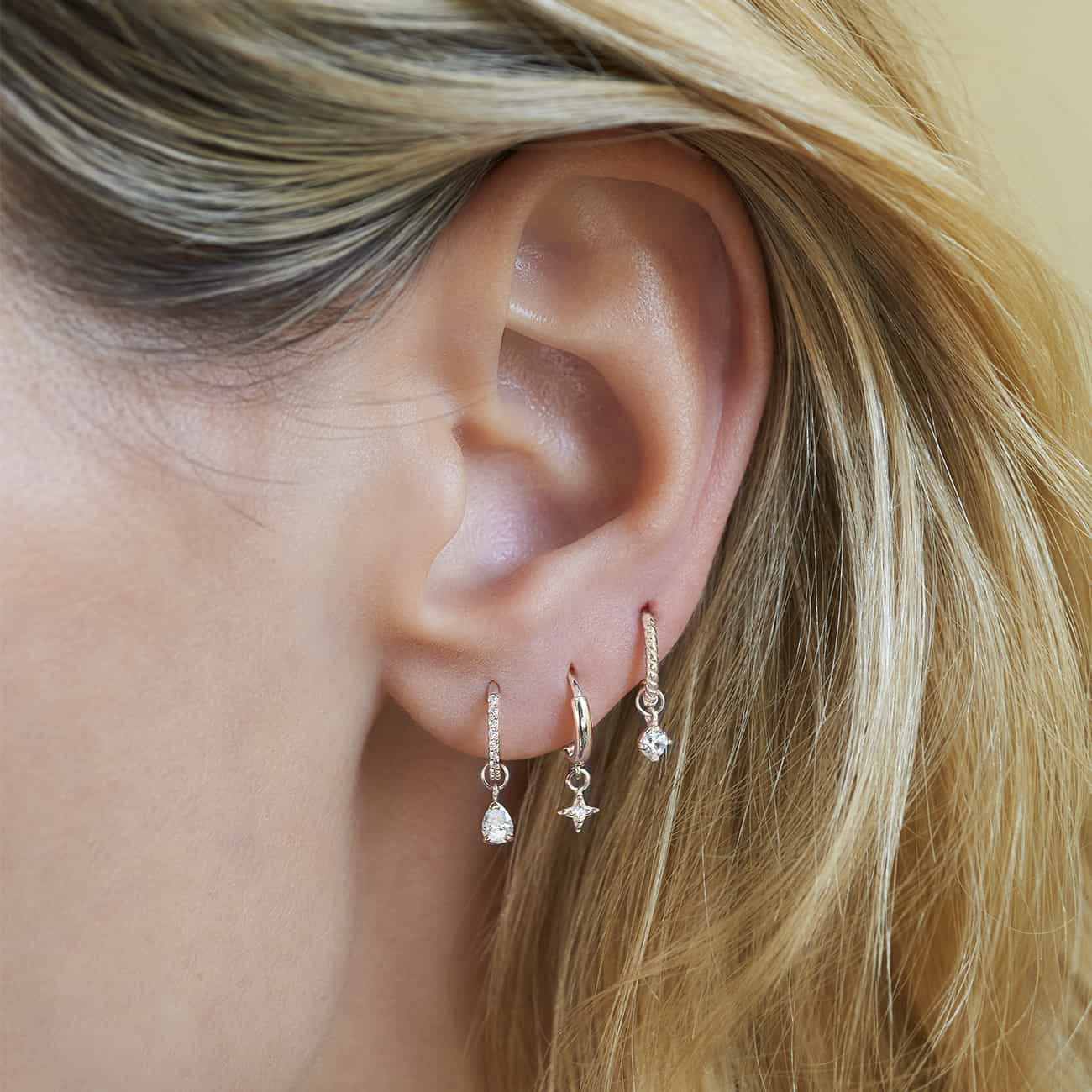 14K white gold moissanite charm on a pave huggie hoop, shown on a model's lobe