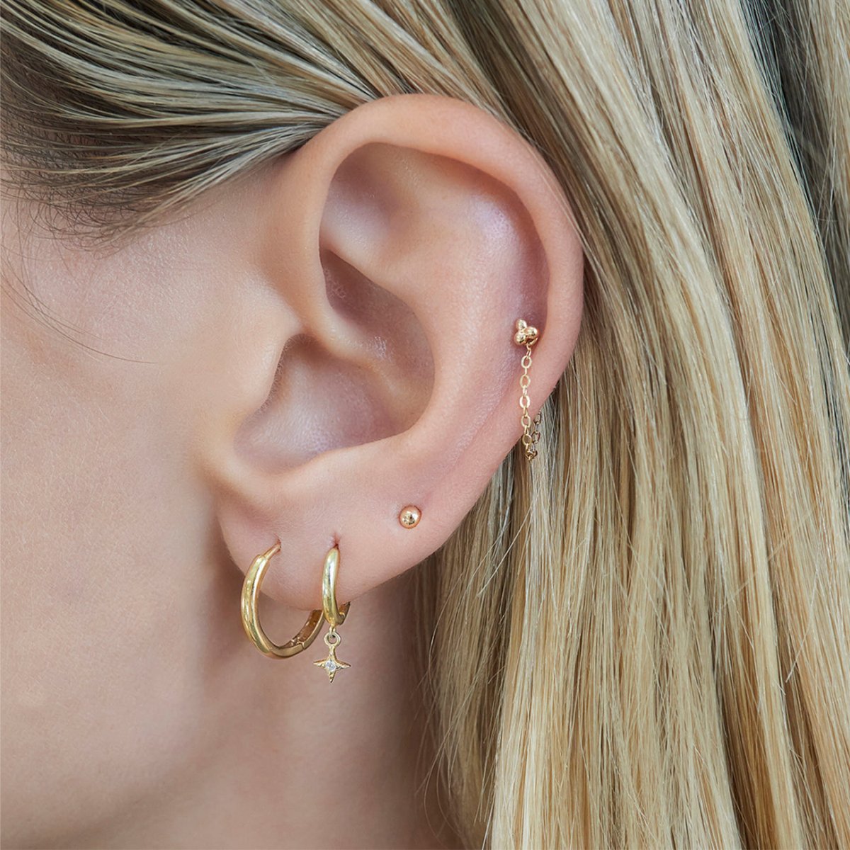 14K gold chain-linked huggie hoops shown stacked on a model's ear