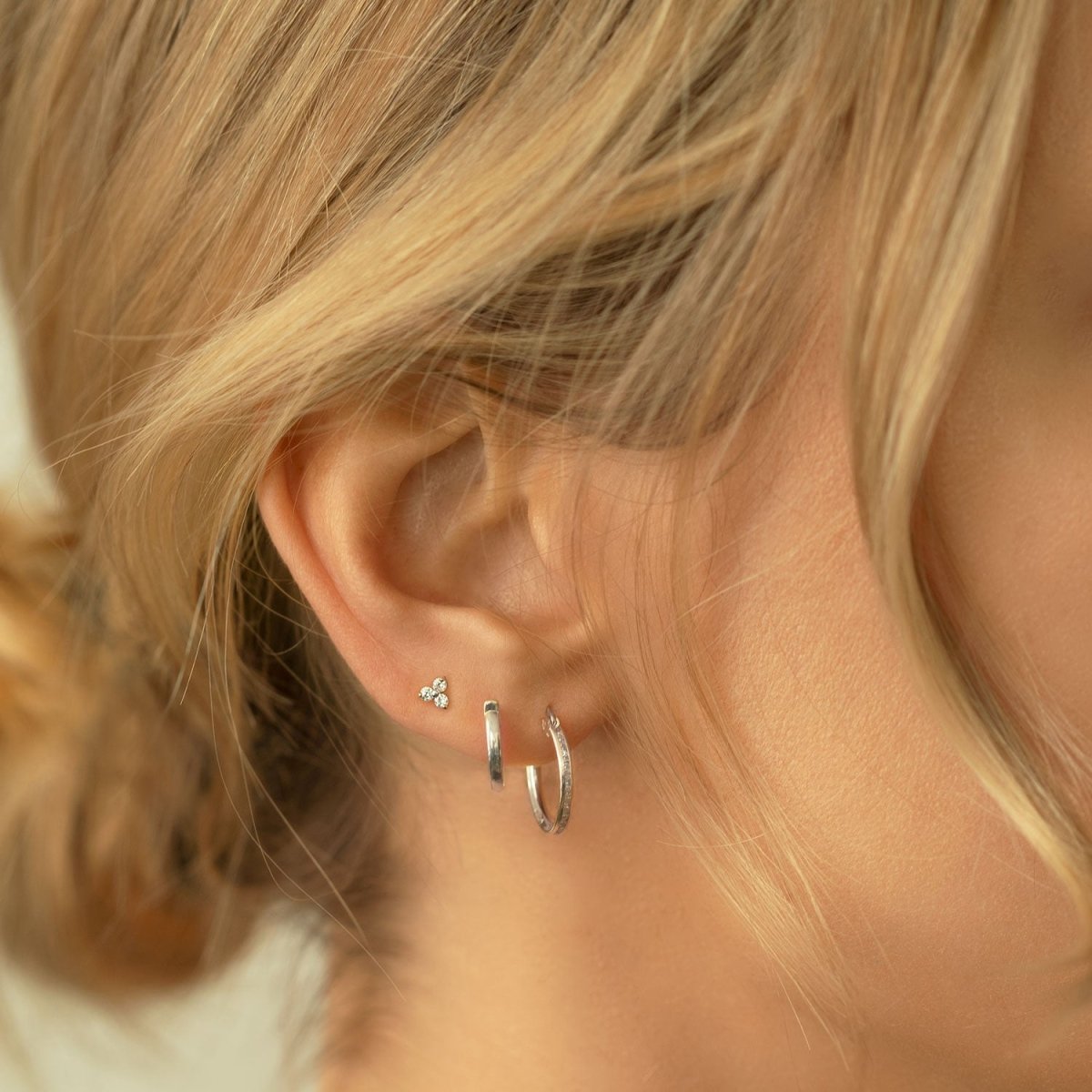 Sterling silver plain huggie hoop shown on a model's ear with a tiny three-stone stud above
