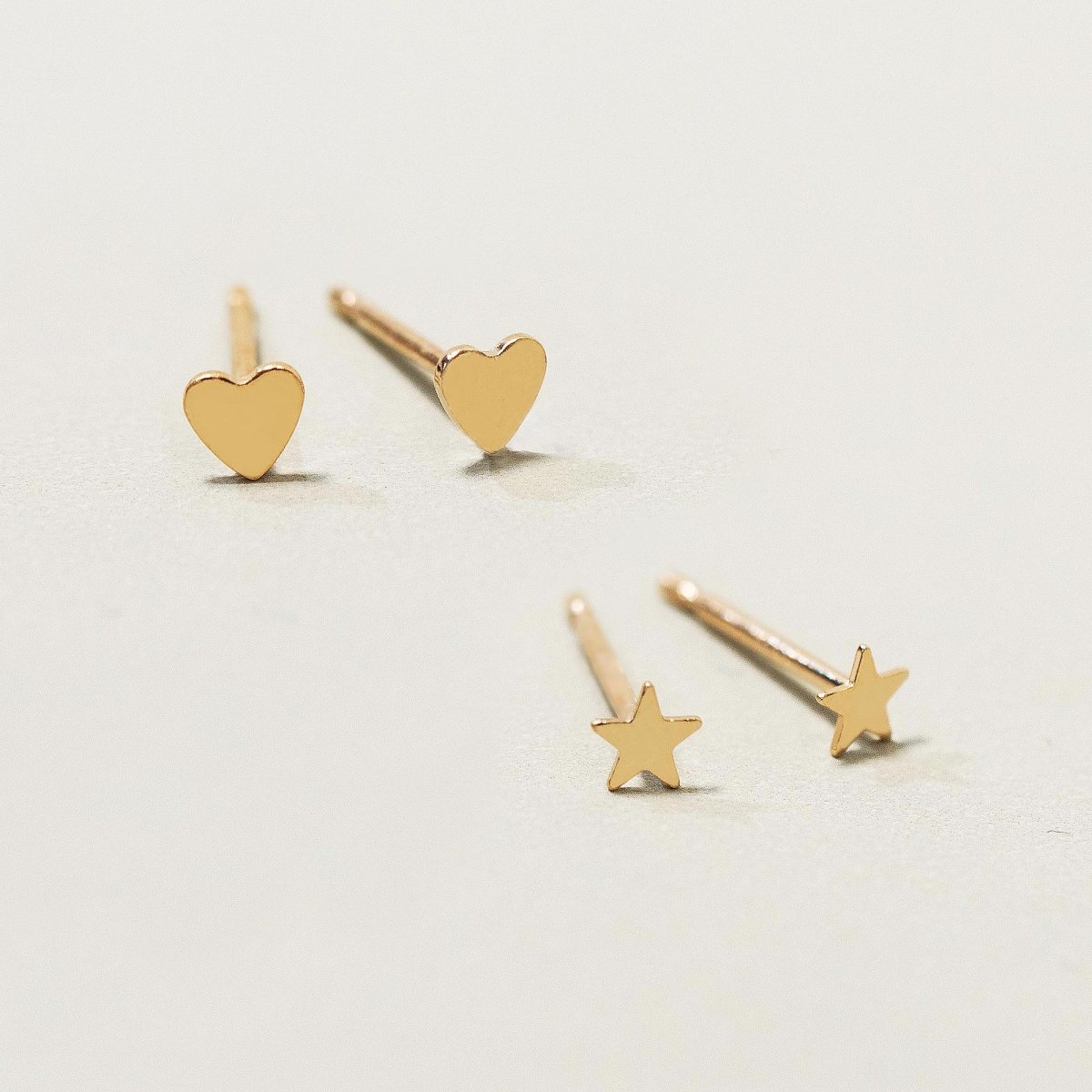 Gold-filled tiny heart and star studs scattered on a cream surface, close-up detail