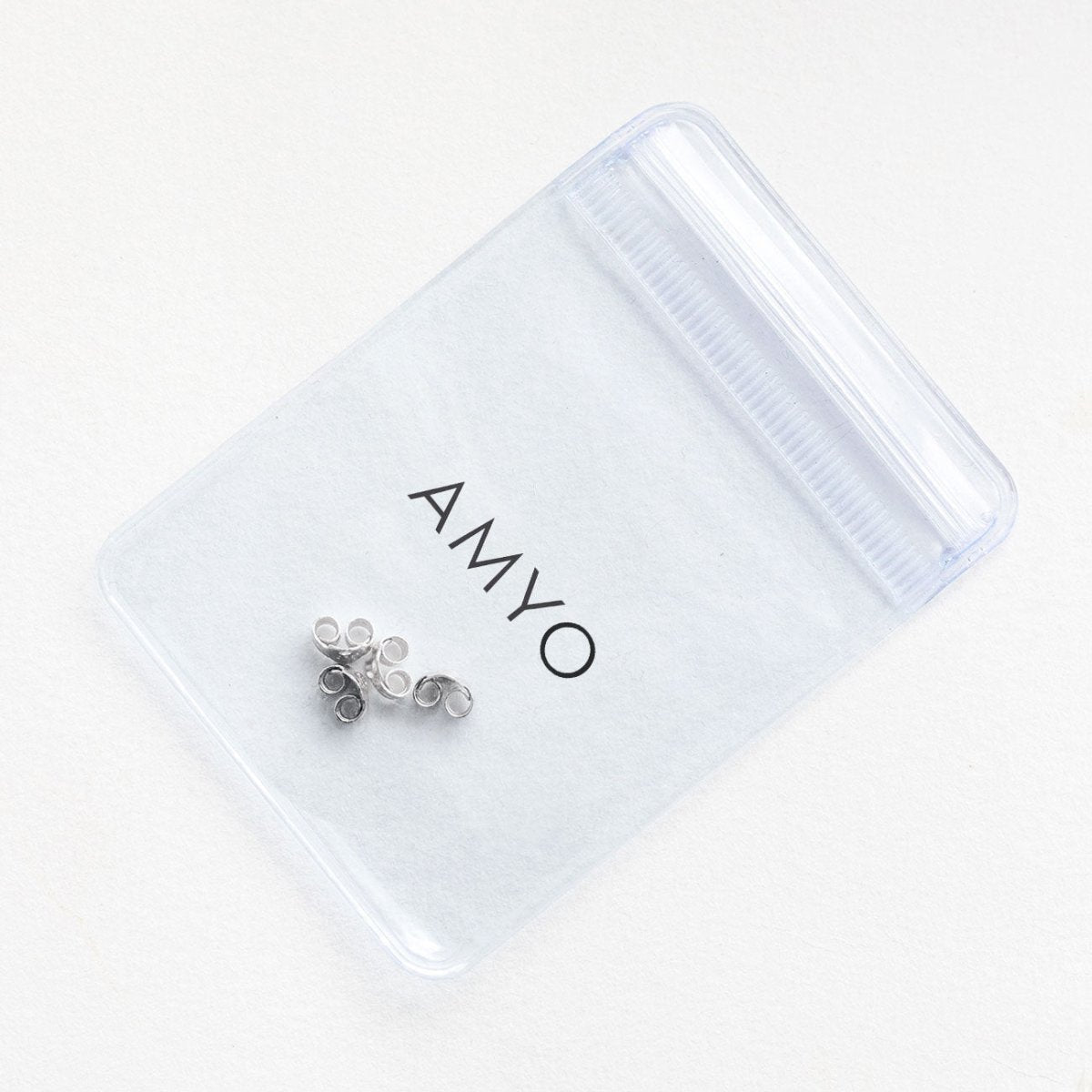 Sterling silver earring backs resting on a frosted AMYO pouch, close-up of friction butterfly backs