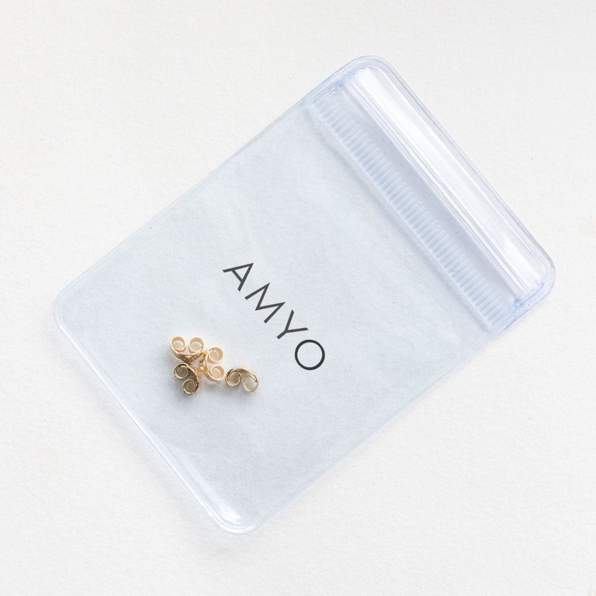 Gold vermeil earring backs resting on a frosted AMYO pouch, close-up of friction butterfly backs