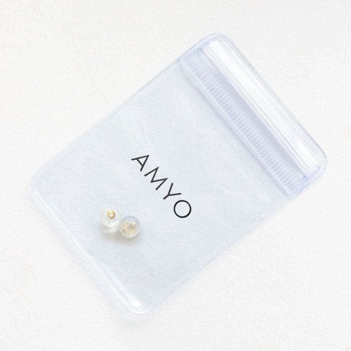 Pair of clear silicone earring backs with a 14K gold core, shown beside an AMYO pouch