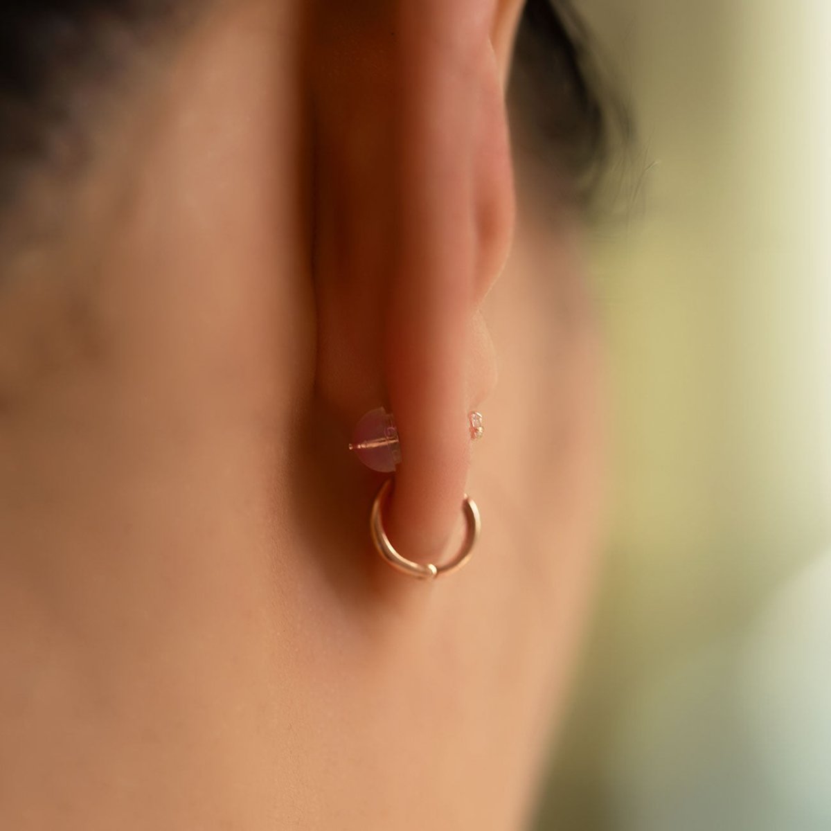 Clear silicone earring back with a 14K rose gold core, close-up behind a model's lobe with a hoop