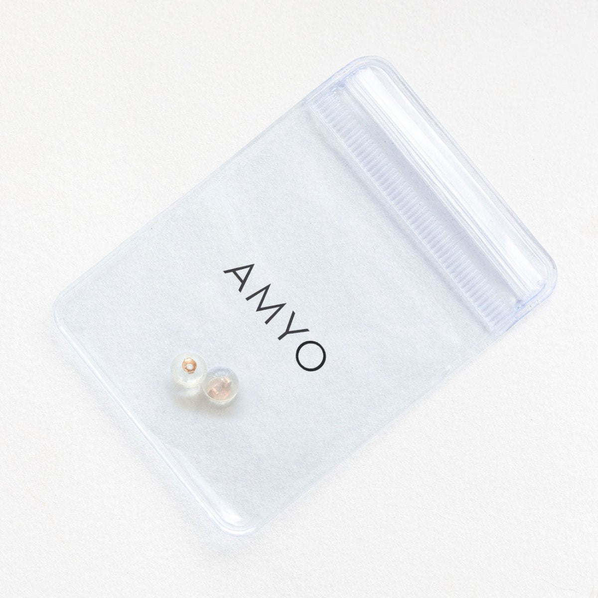 Pair of clear silicone earring backs with a 14K rose gold core, shown beside an AMYO pouch