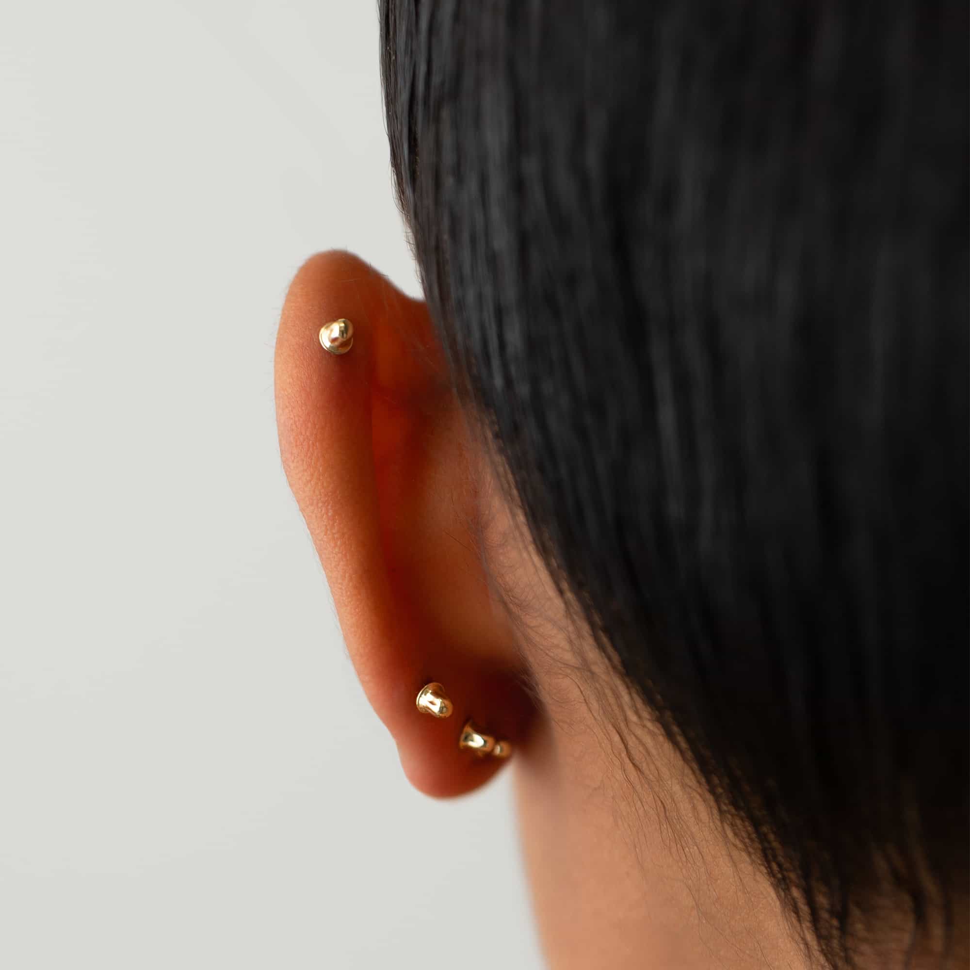 14K gold screw-back earring backs shown securing studs on a model's lobe and helix