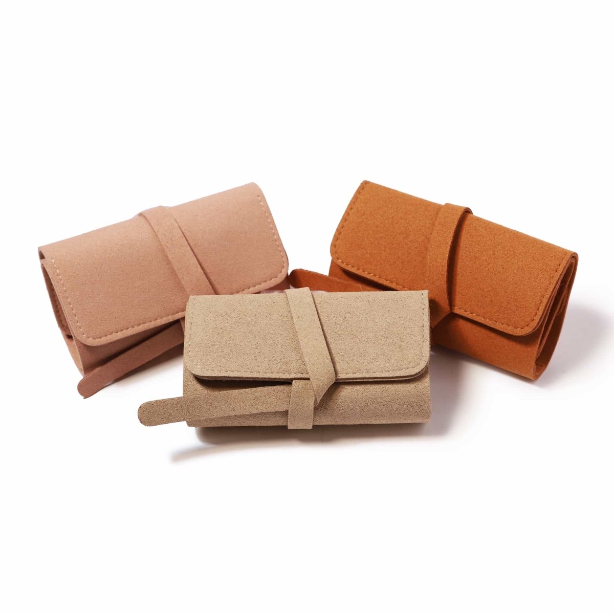Three travel jewelry rolls in pink, rust, and tan suede grouped, on a white background