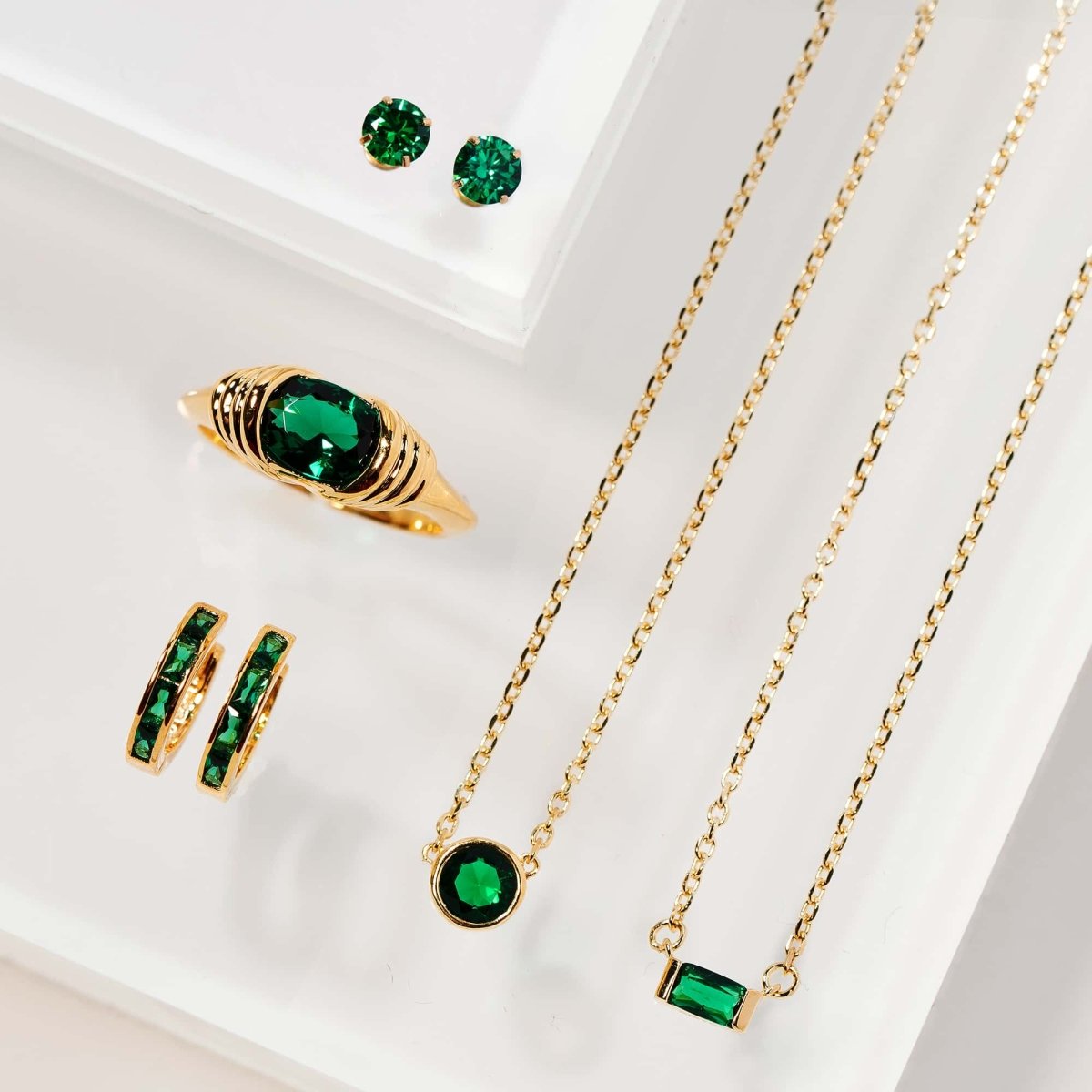 Gold vermeil emerald jewelry set with round studs, a ring, huggies and bezel pendant, on a white background