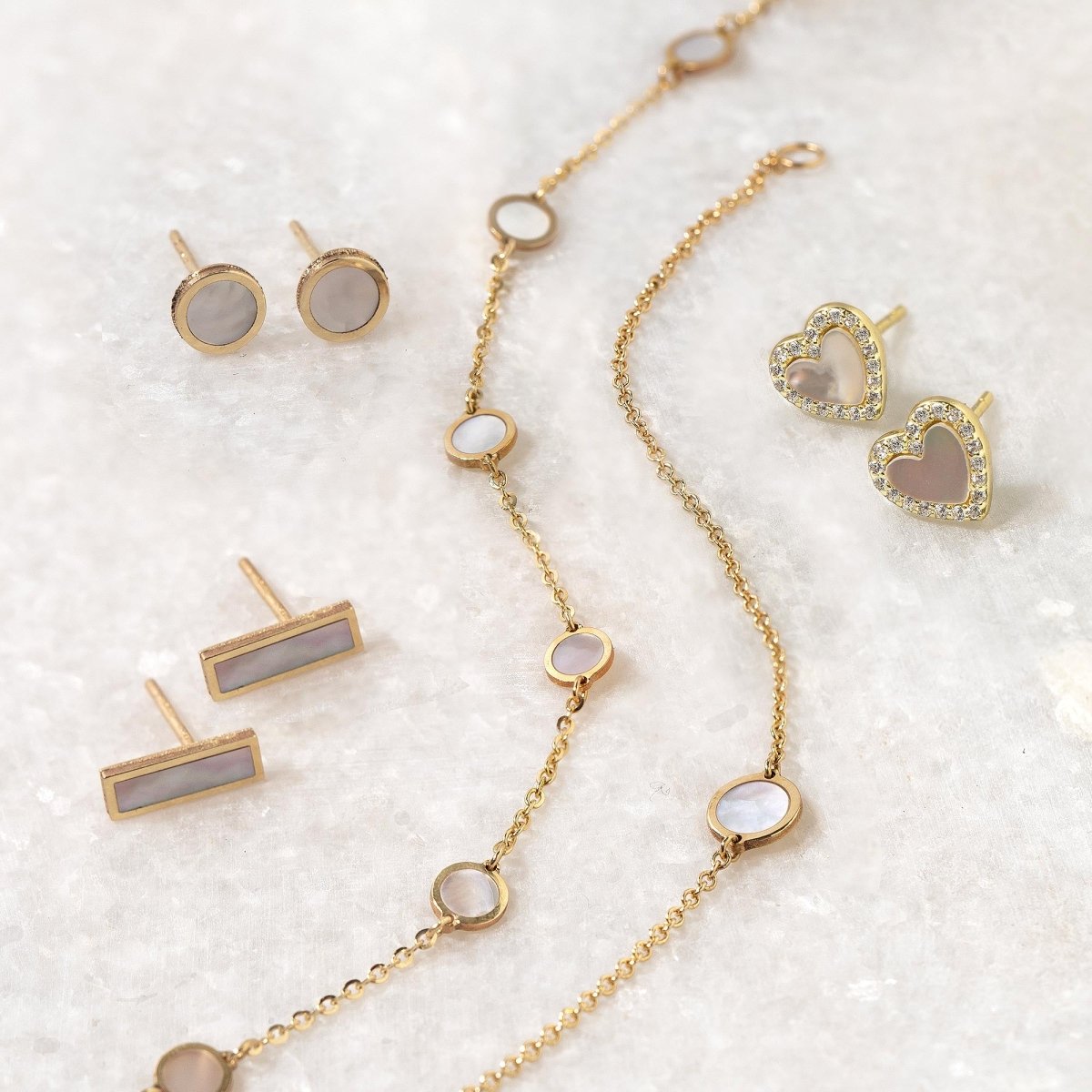 Gold vermeil mother of pearl heart studs styled with bar studs and a station necklace on a white background